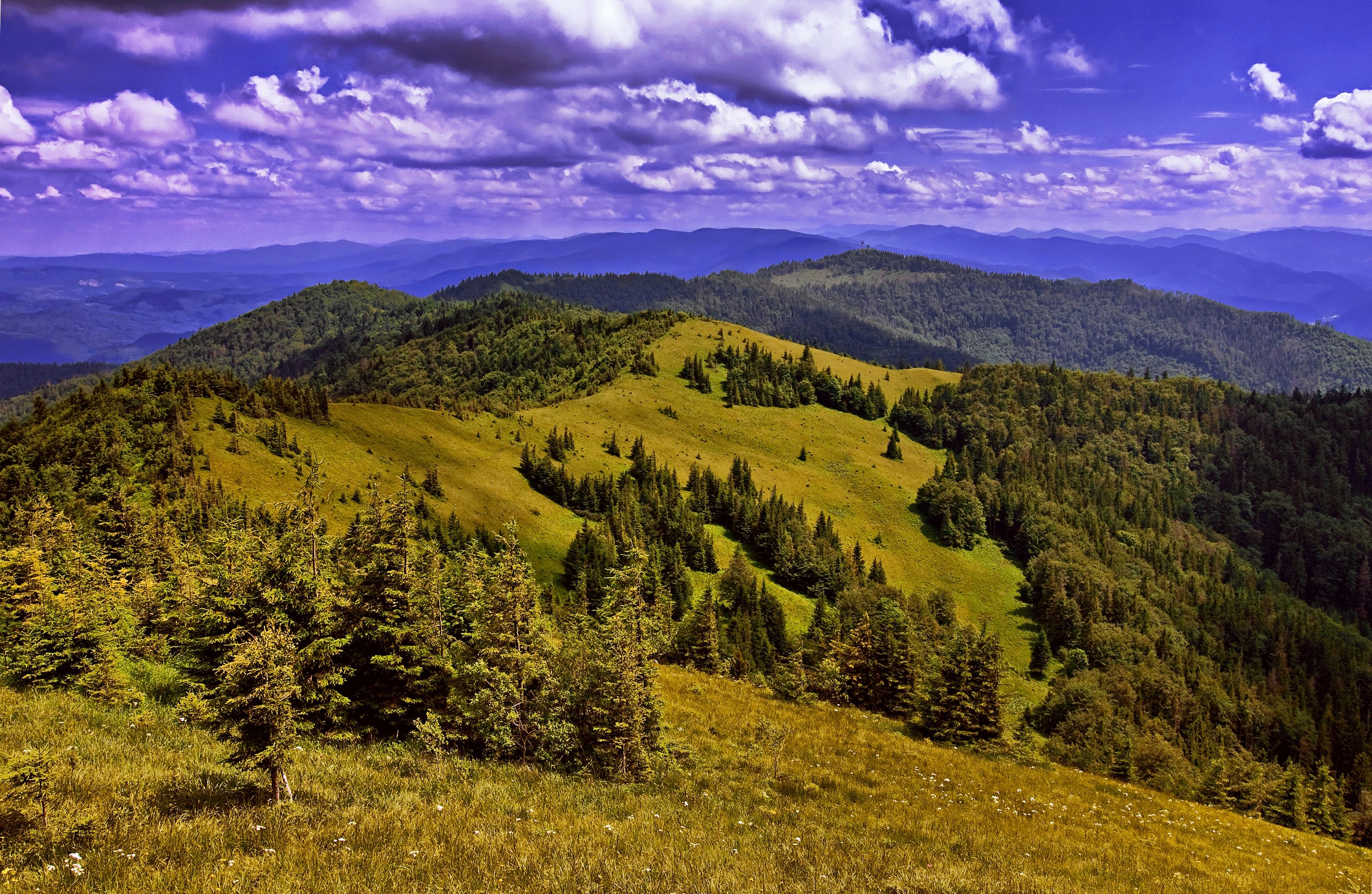 Mountain range with green hills and forests under a cloudy sky HD Wallpaper