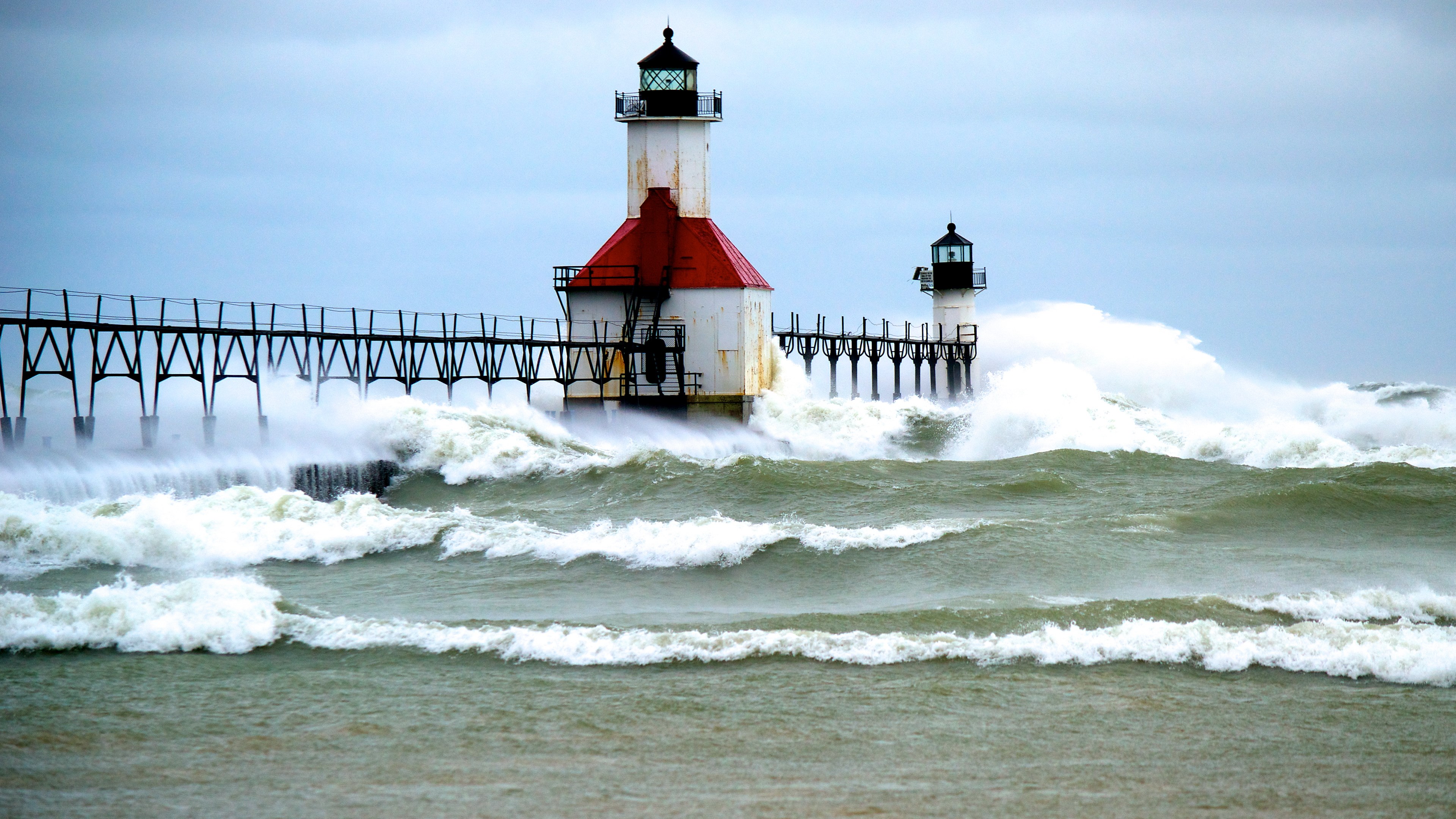 Two lighthouses on a pier during a storm with large waves HD Wallpaper