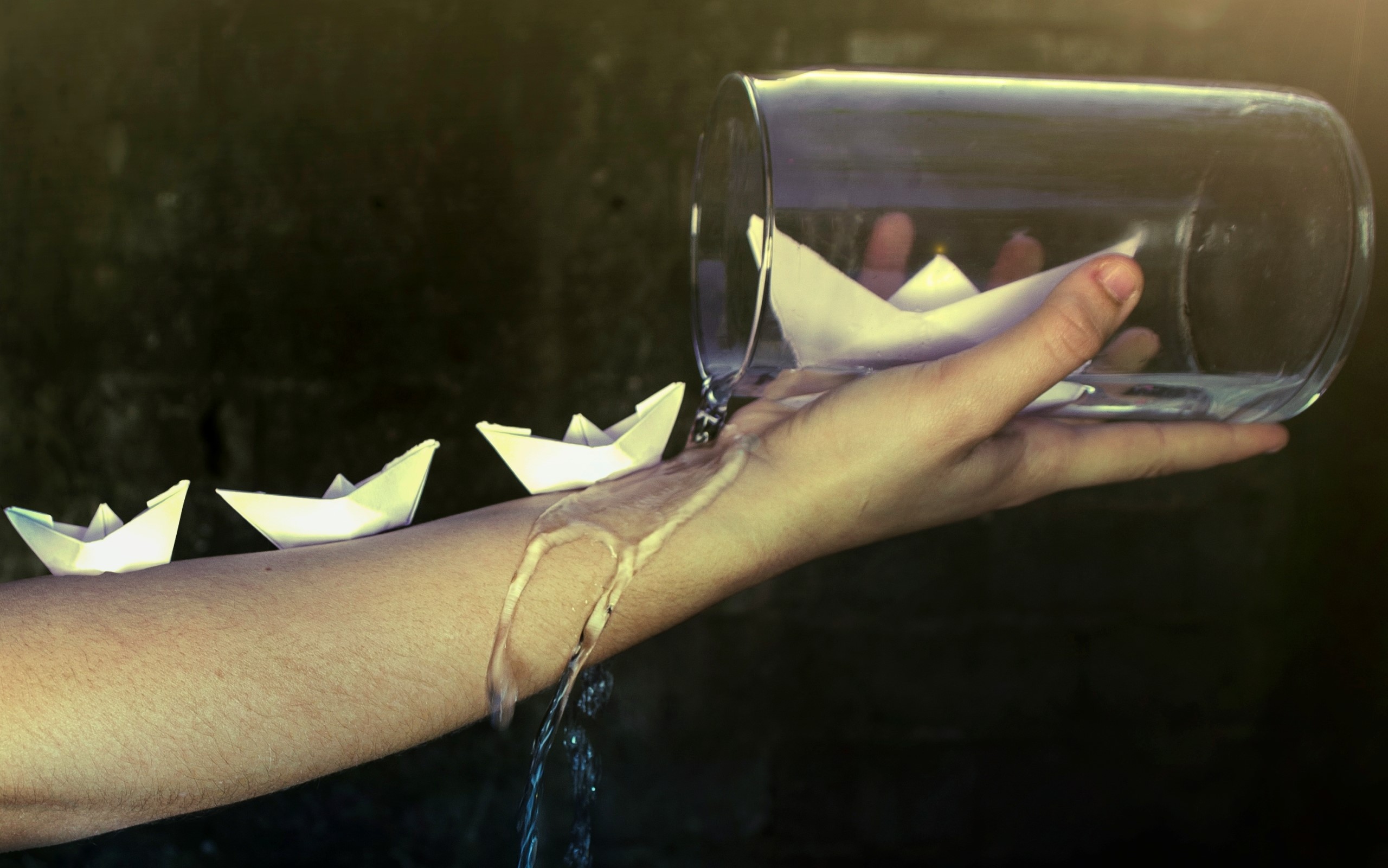 Paper boats floating on a person's arm with water pouring from a jar HD Wallpaper