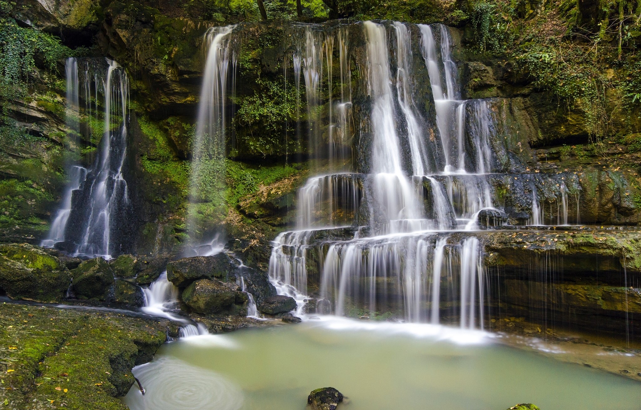 Cascading waterfalls in a lush forest HD Wallpaper