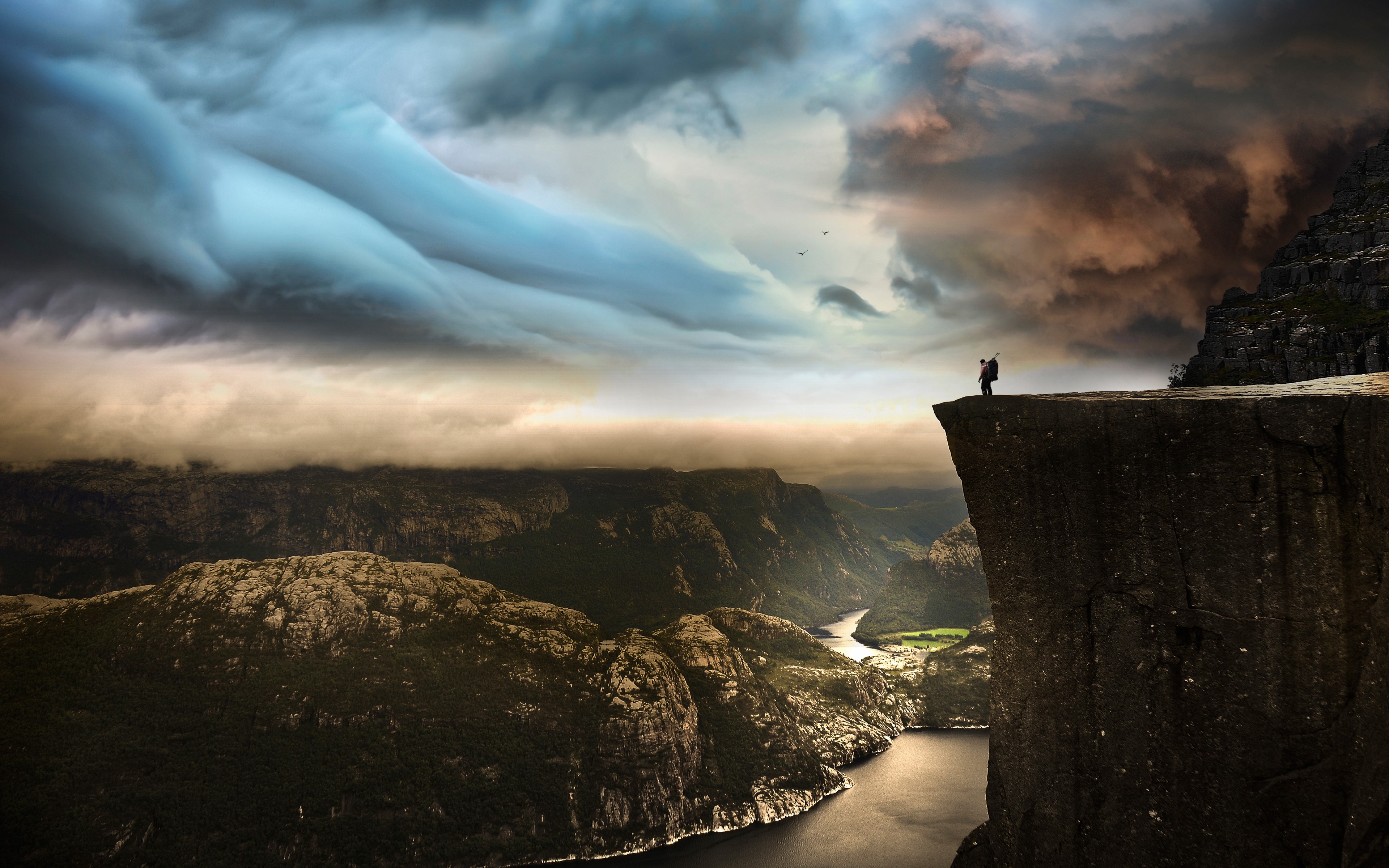Man on cliff edge overlooking fjord in Norway HD Wallpaper