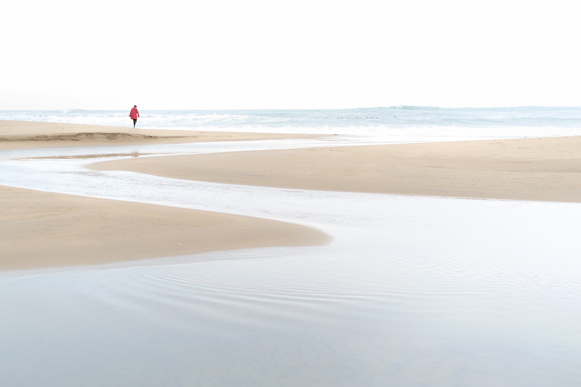 Person in red coat walking on a beach by the sea HD Wallpaper
