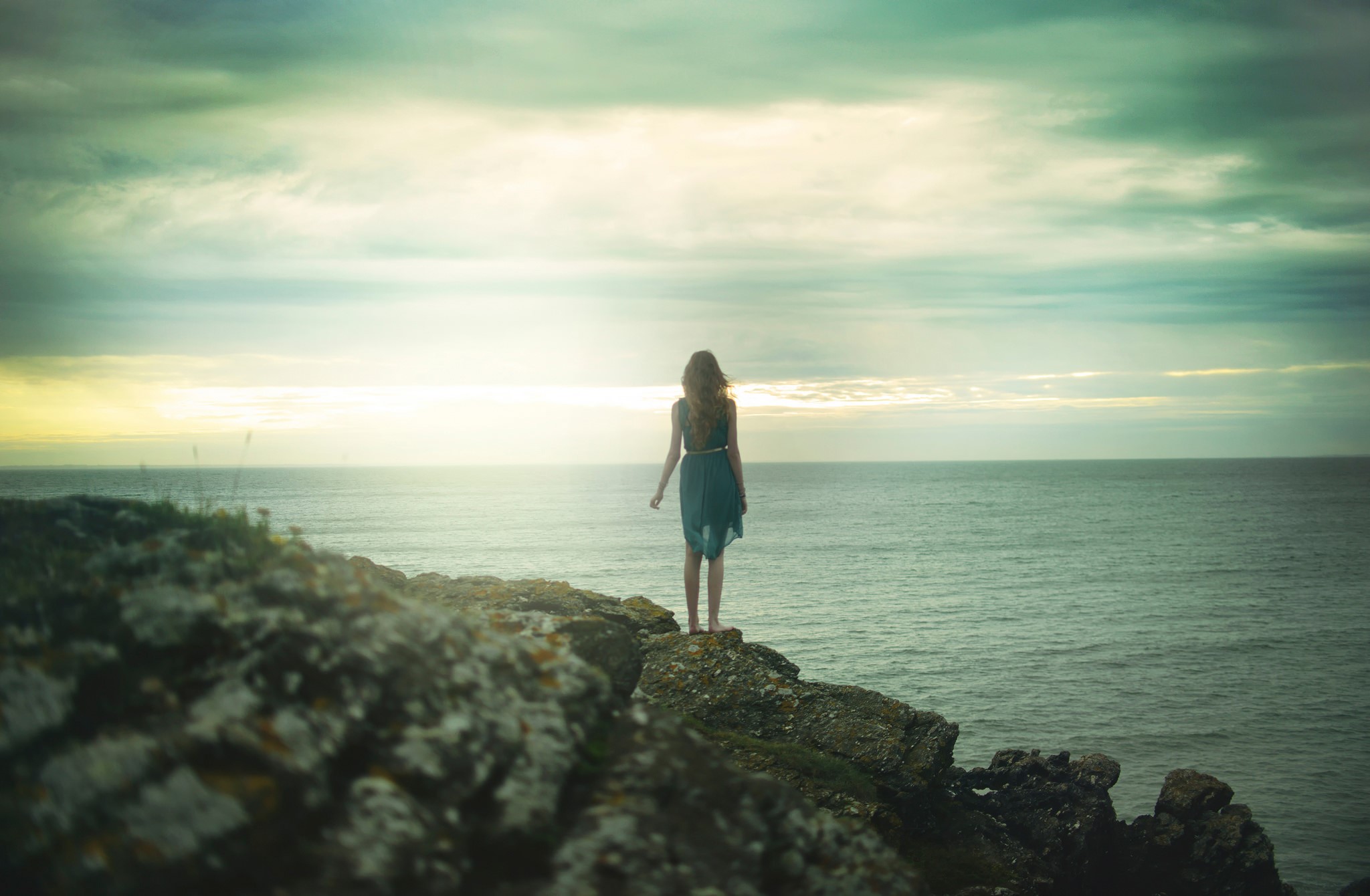 Woman in dress standing on a crag overlooking the sea HD Wallpaper