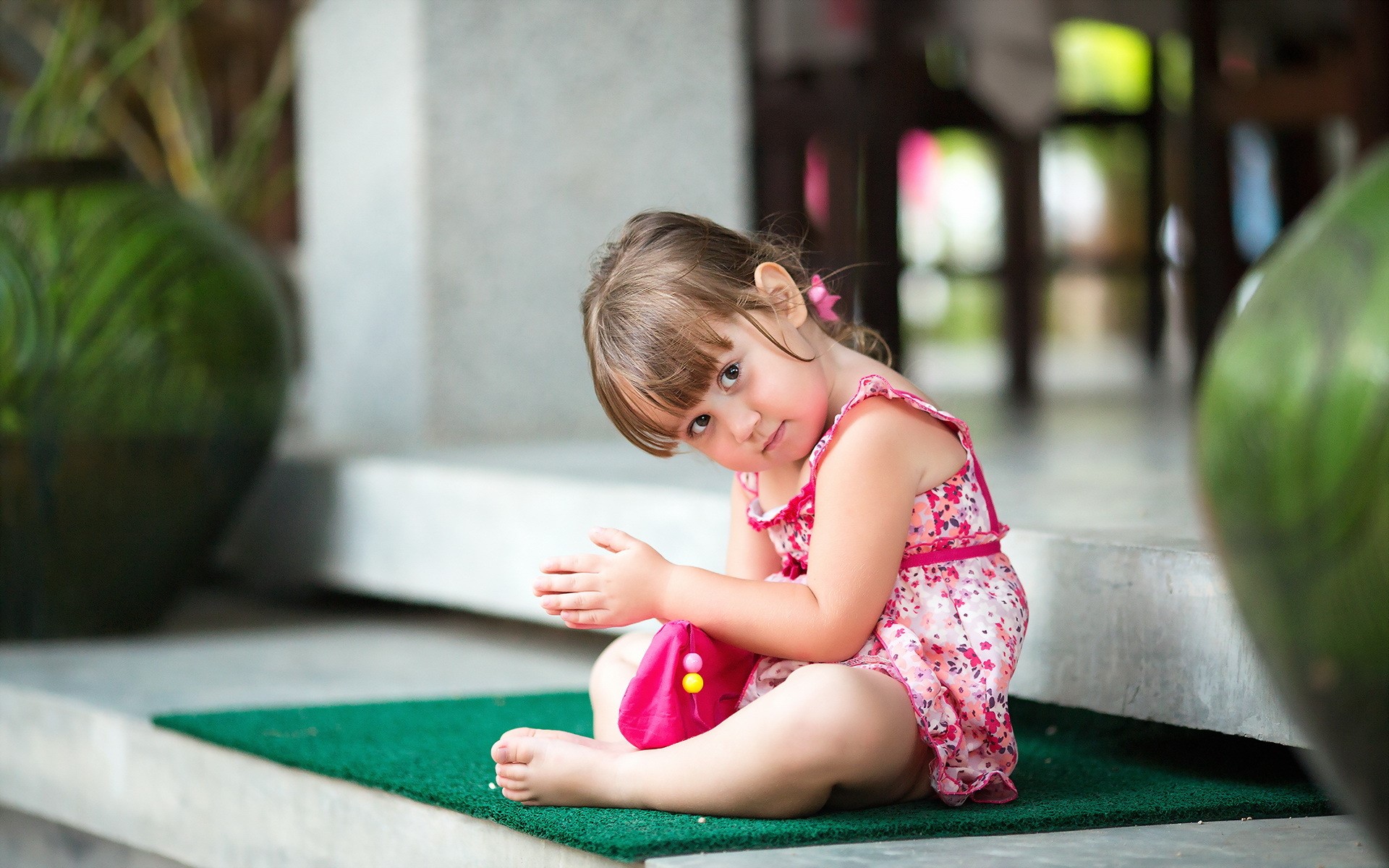 A young girl in a pink dress sits on a green mat HD Wallpaper