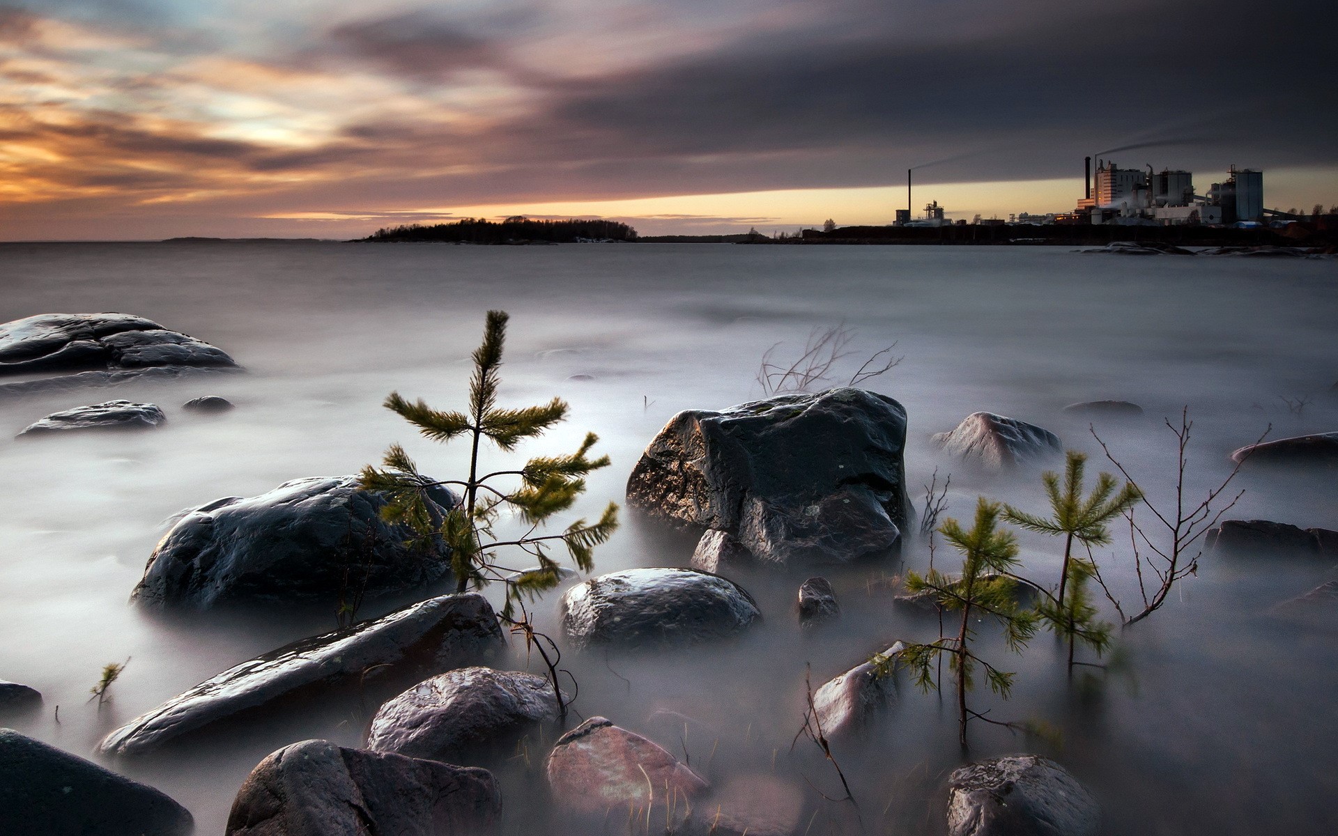 Rocky shore with industrial background at sunset HD Wallpaper