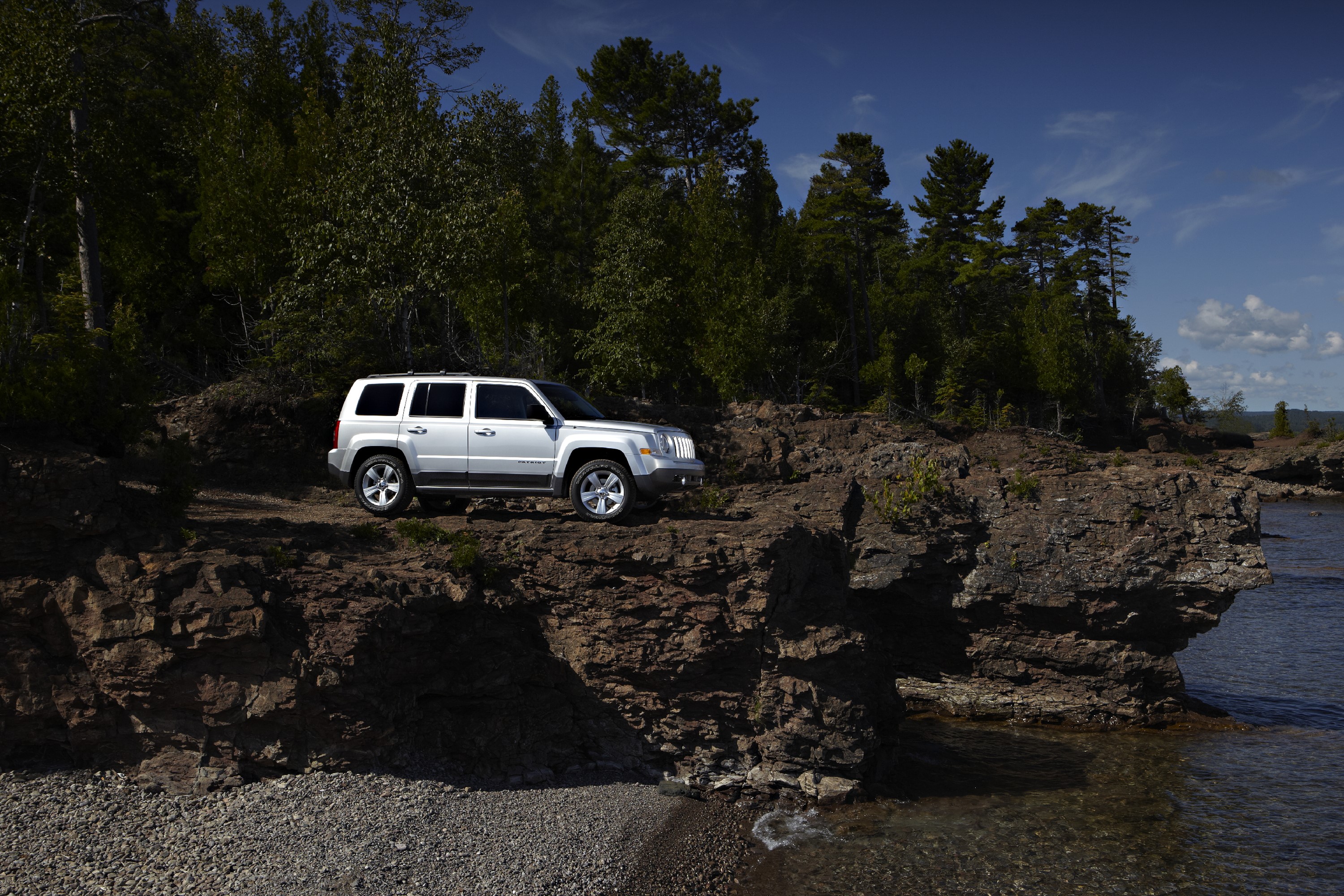 White Jeep Patriot on a rocky coast with forests HD Wallpaper