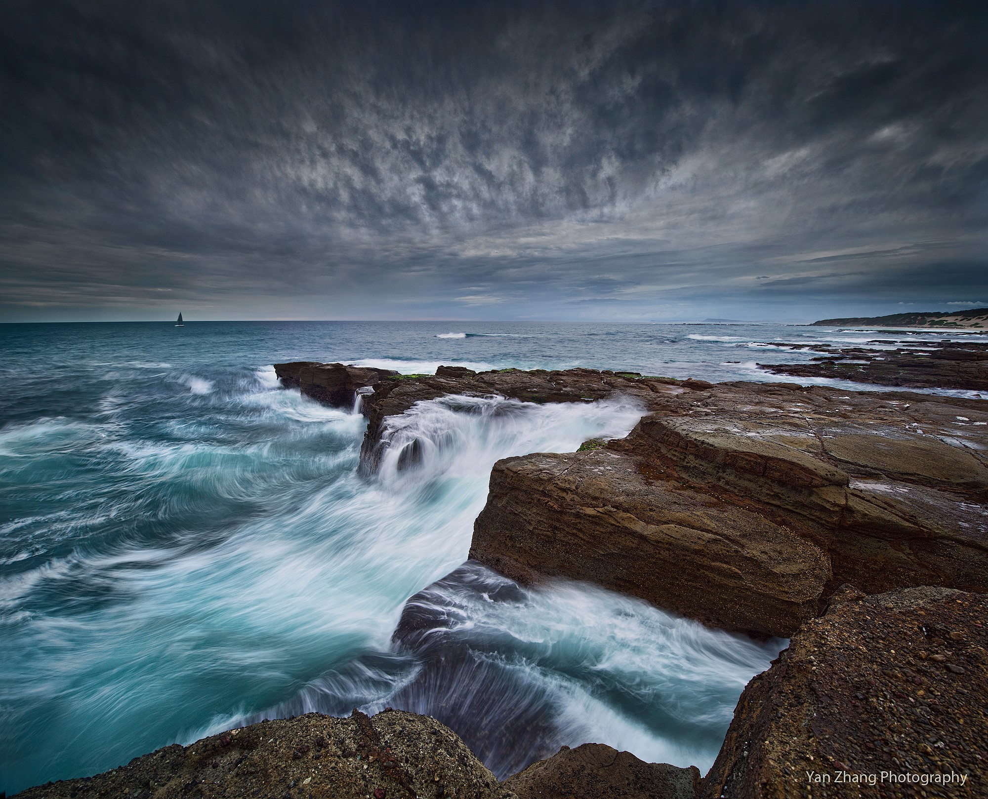 Waves crashing on rocky shore with sailboat HD Wallpaper