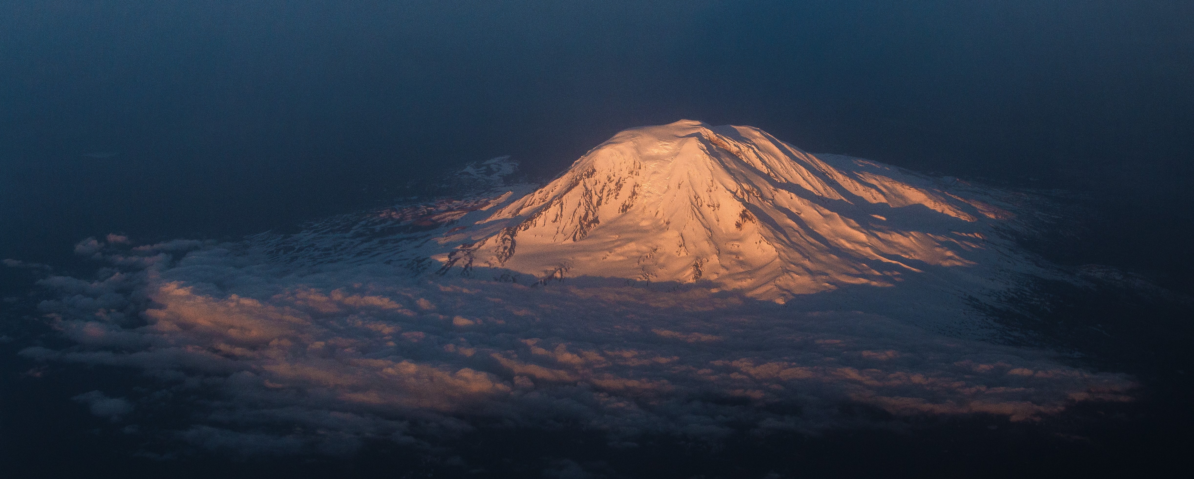 Snow-capped mountain peak above clouds at sunrise HD Wallpaper