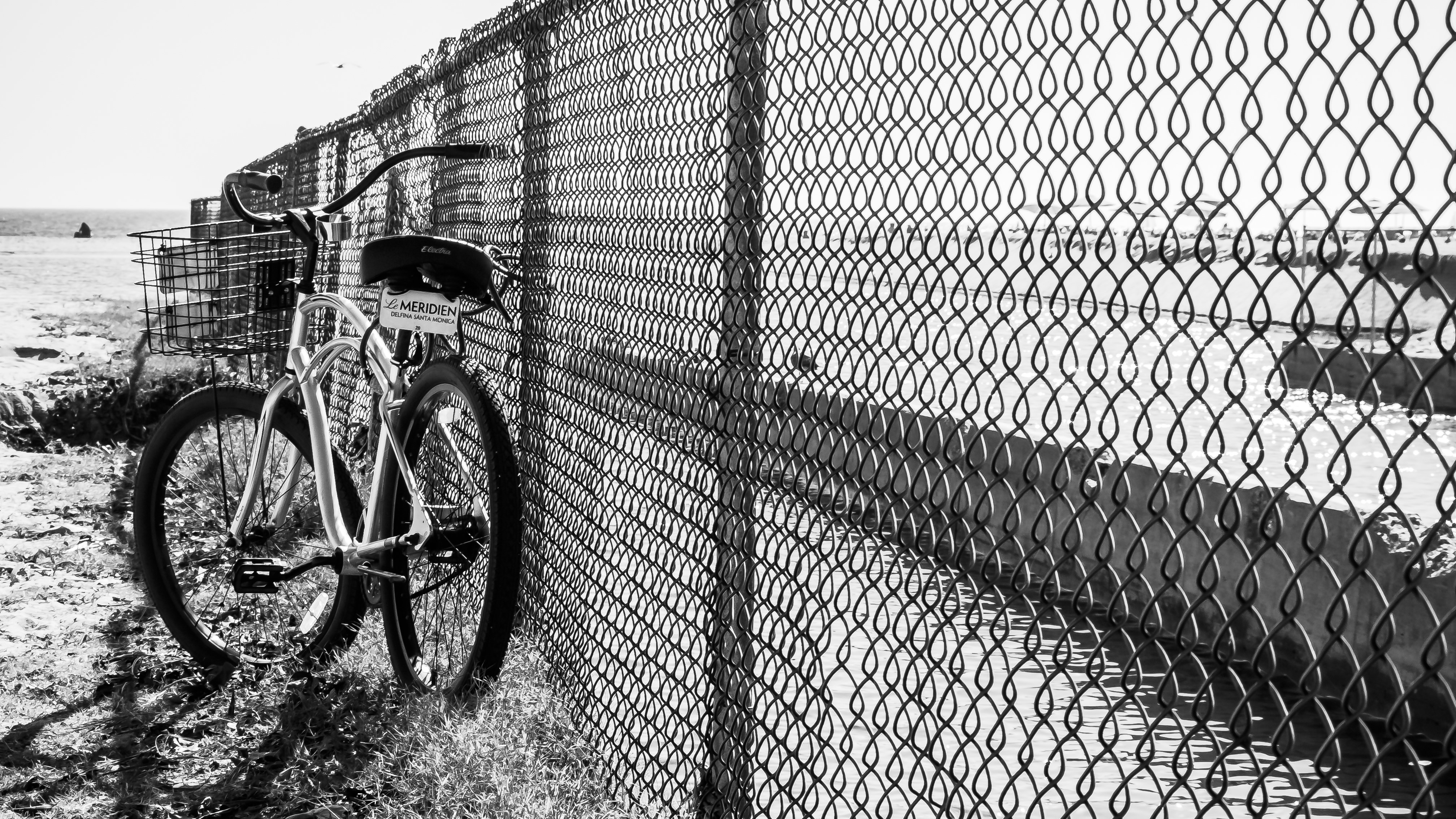 Bicycle leaning against a chain-link fence at the beach HD Wallpaper