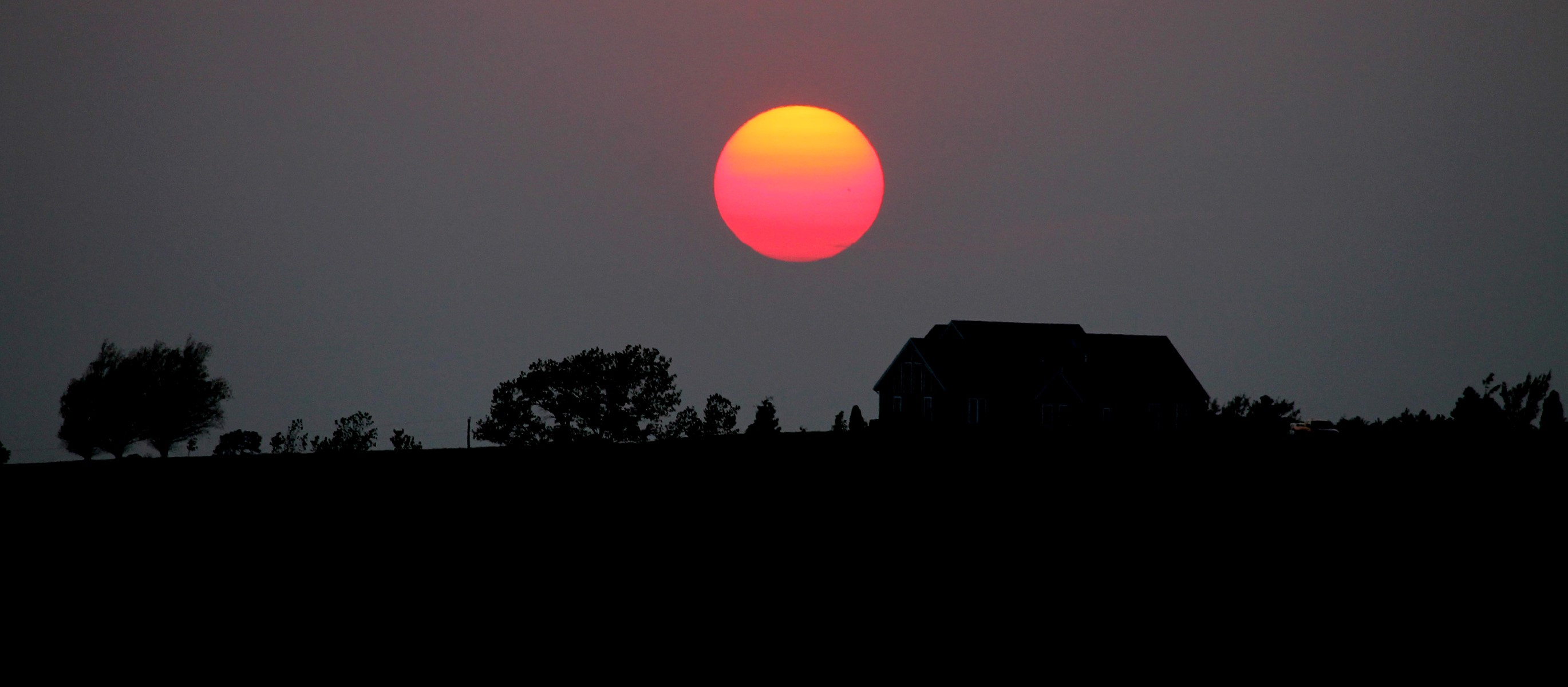 Sunset over a silhouetted landscape with a house HD Wallpaper