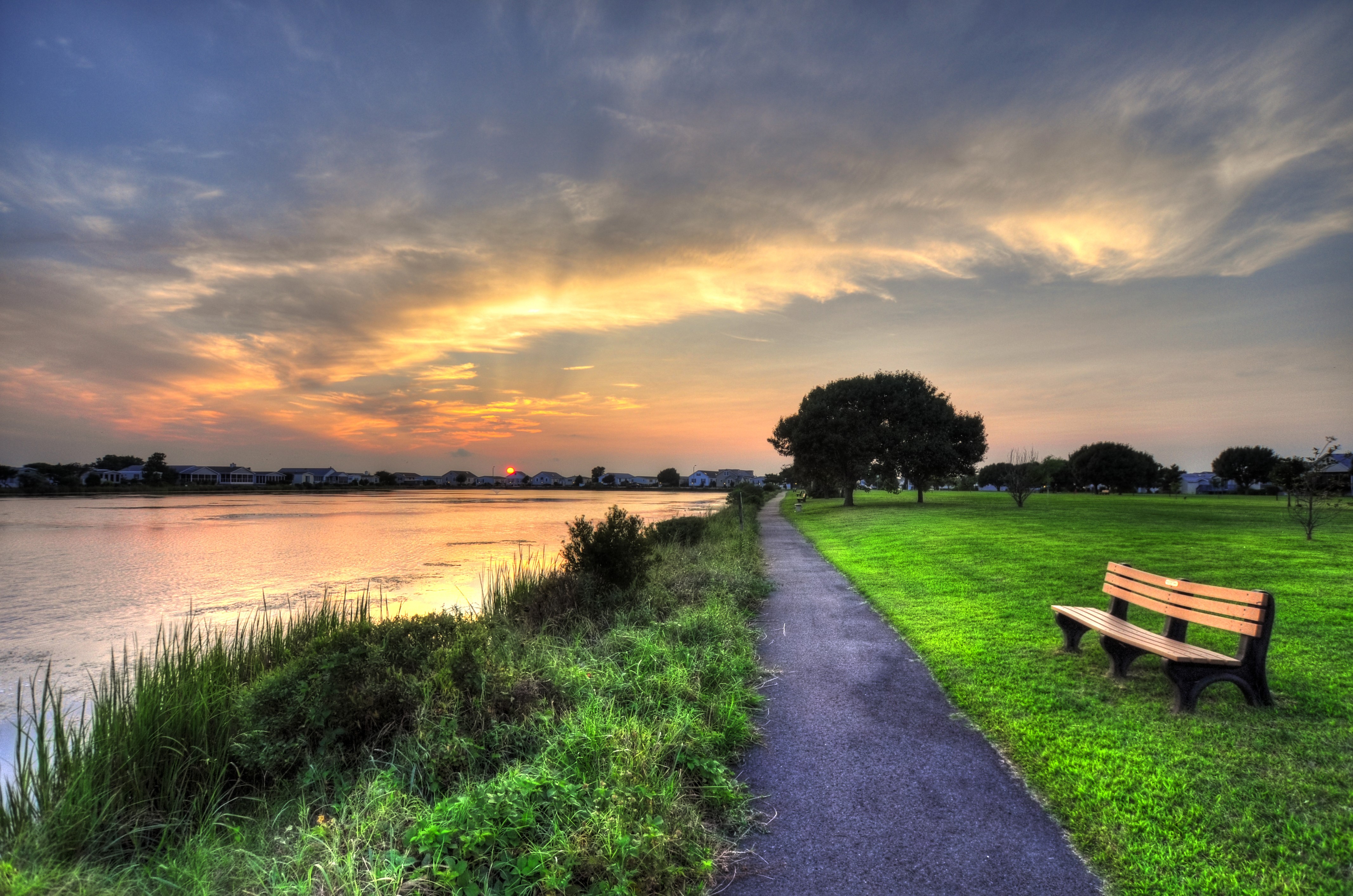 Park trail by lake at sunset with bench HD Wallpaper