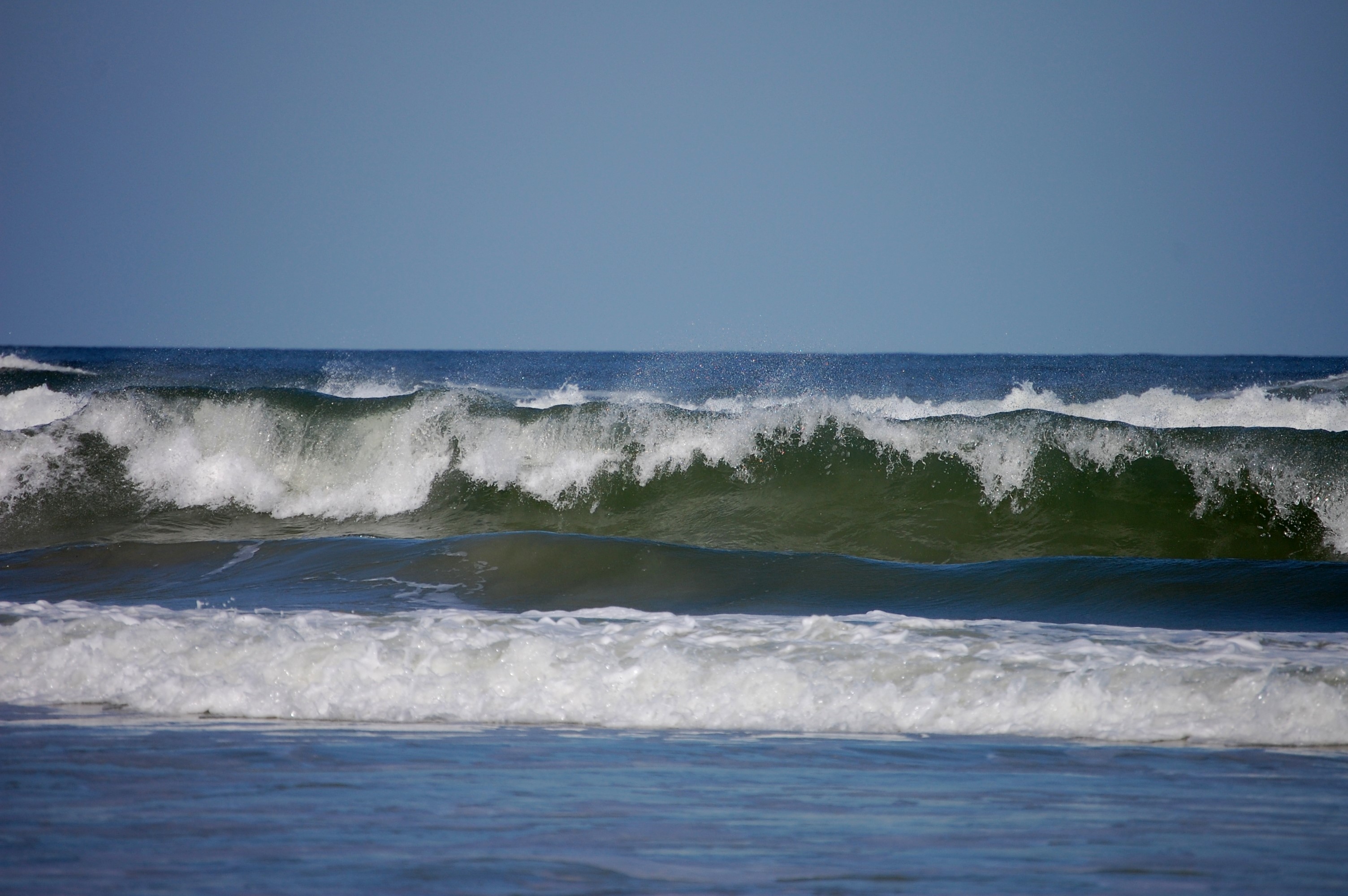 Ocean waves crashing under a clear blue sky HD Wallpaper
