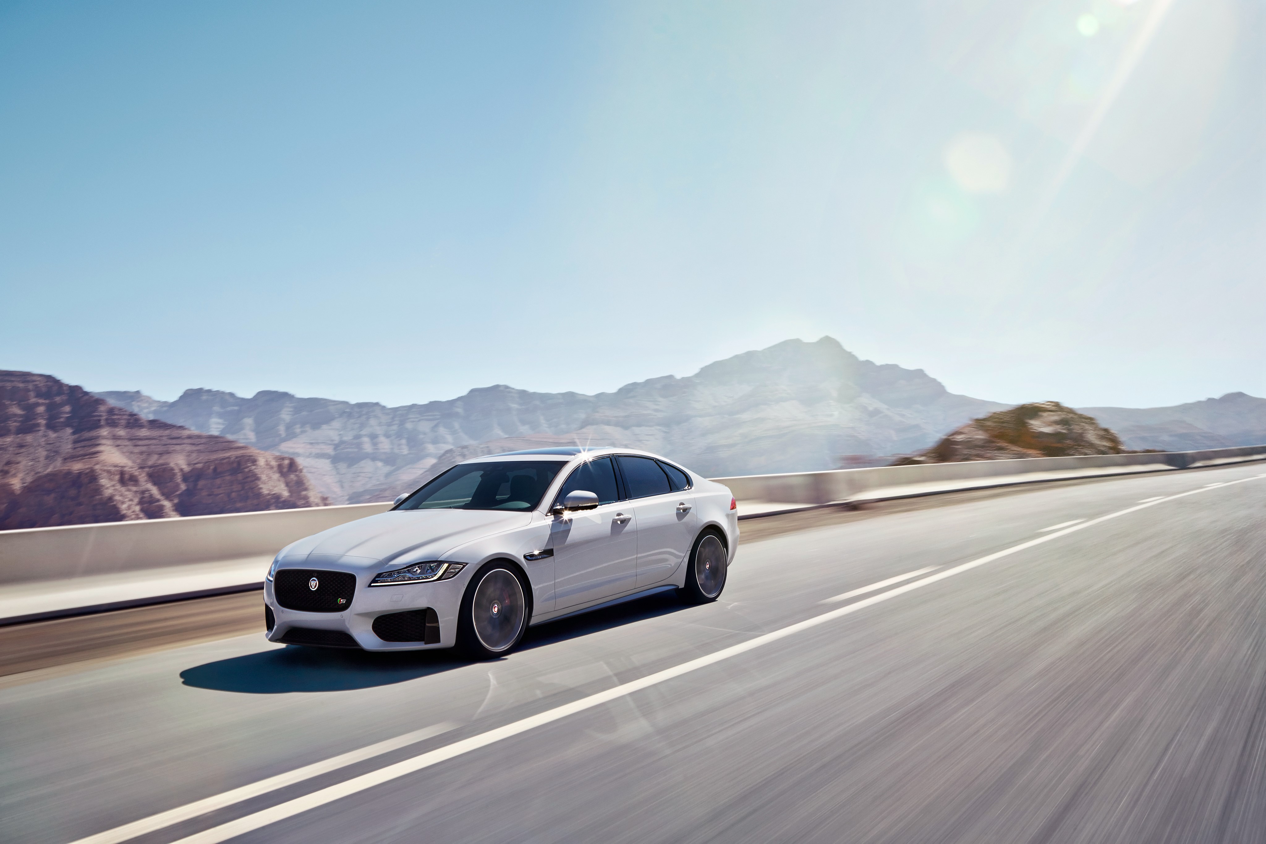 2015 Jaguar XF S AWD driving on a road with mountains HD Wallpaper