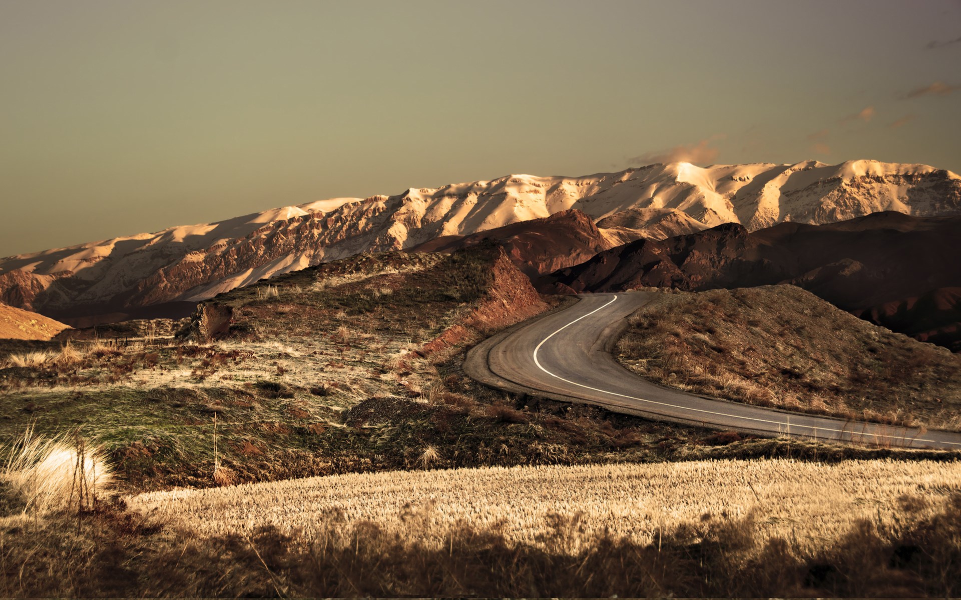 Winding road through mountainous landscape with snow-capped peaks HD Wallpaper