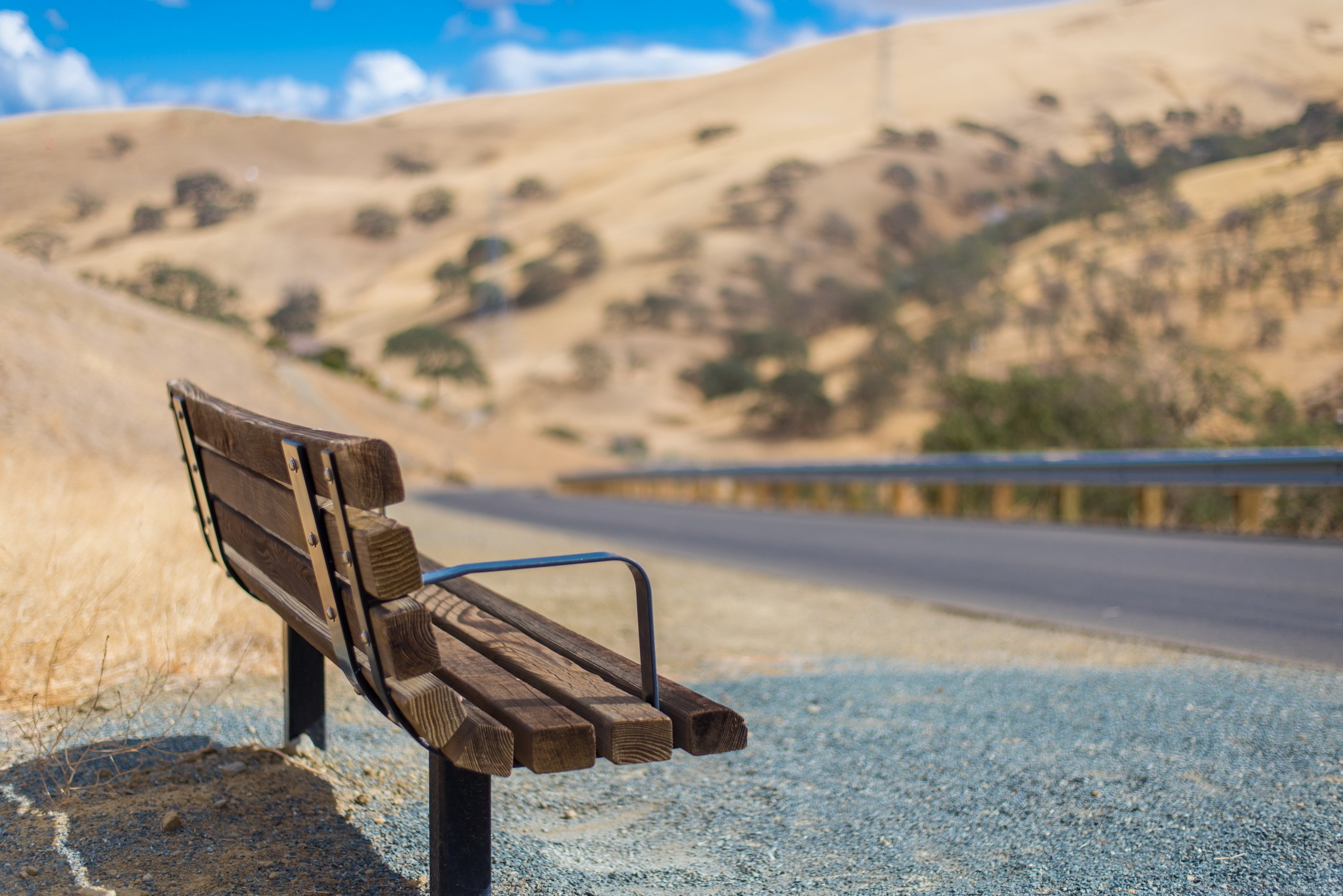 Wooden bench by a road in a dry landscape HD Wallpaper