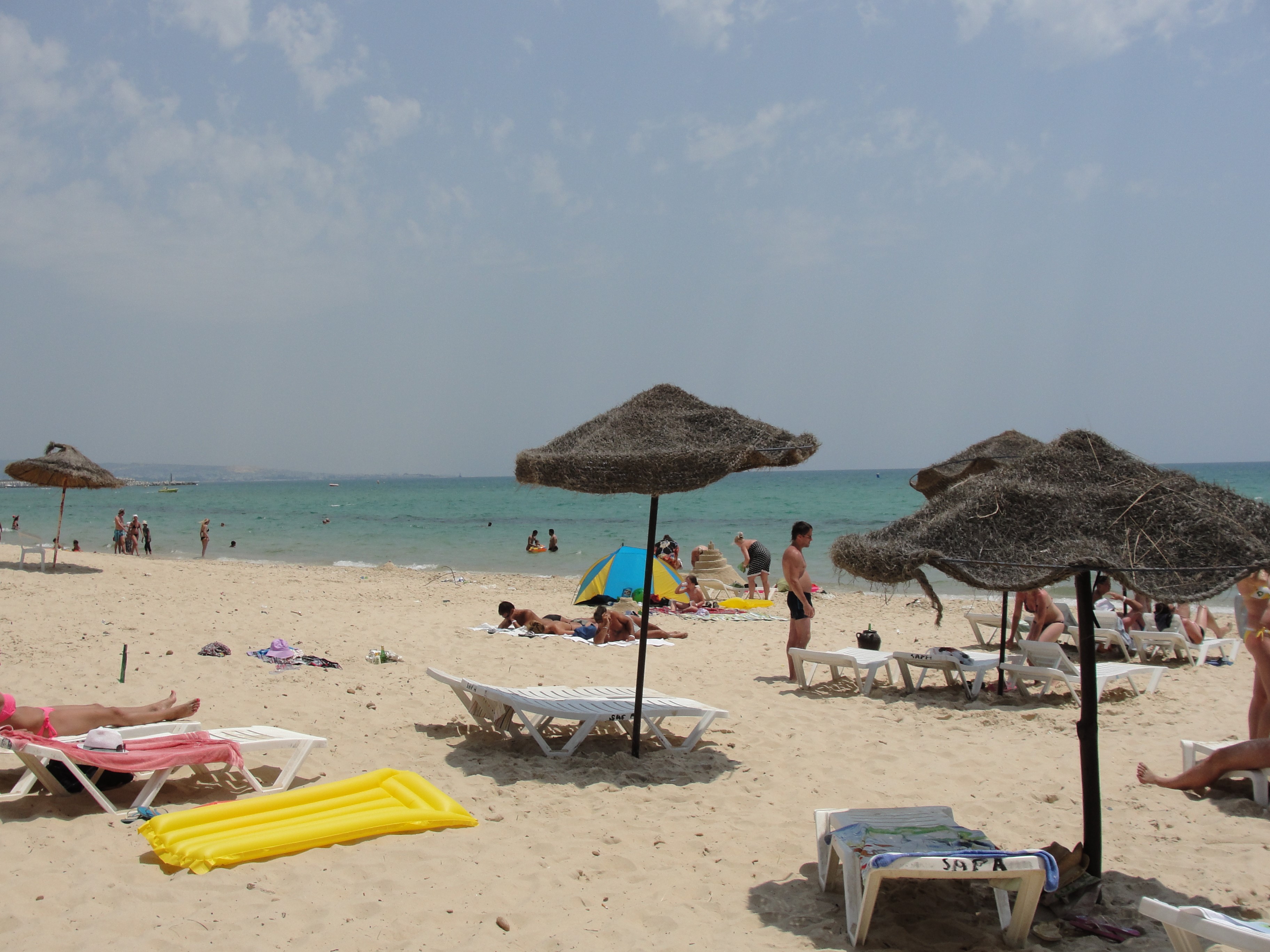 Beach umbrellas and people relaxing on the sand in Hammamet, Tunisia HD Wallpaper