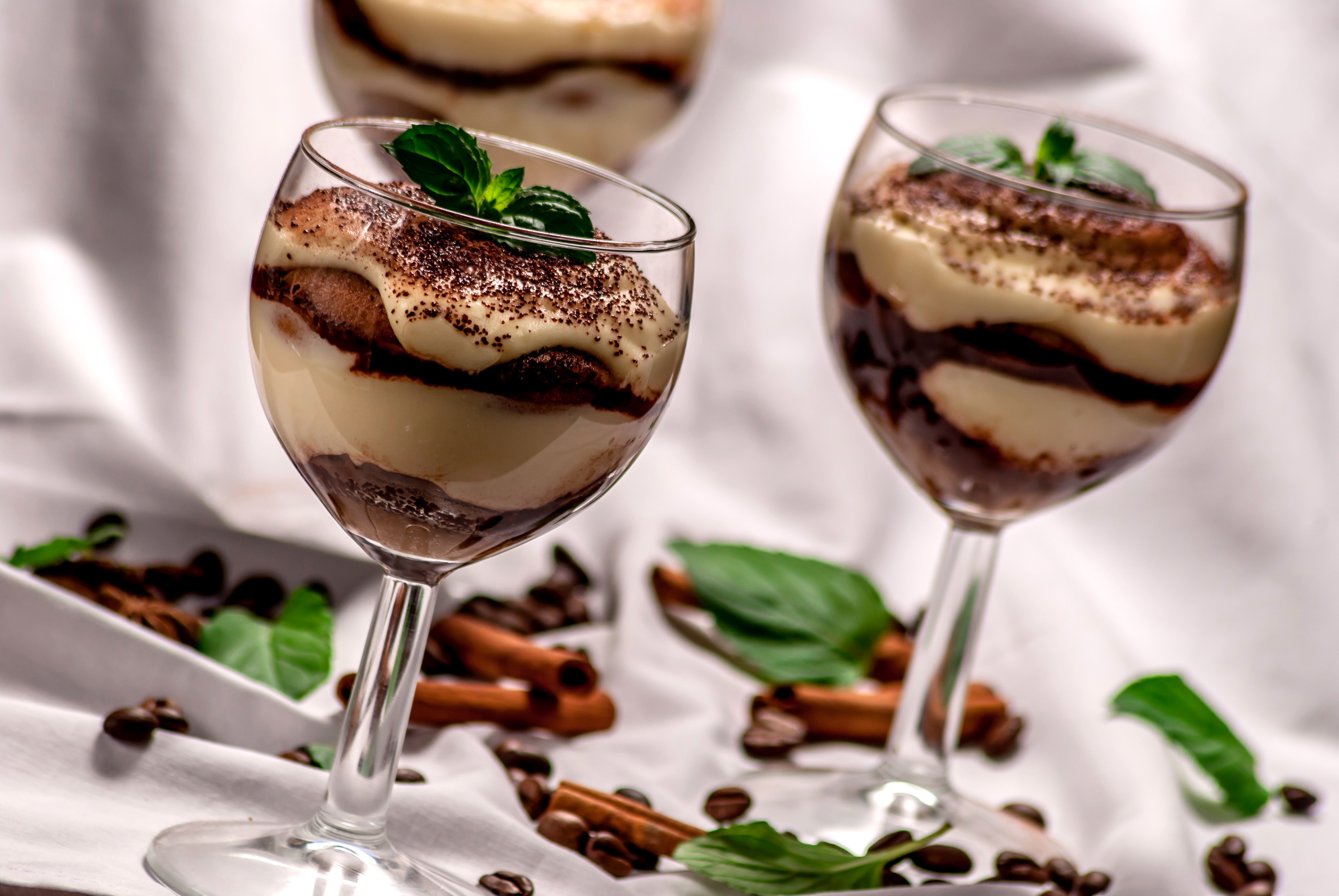 Tiramisu desserts in wine glasses with coffee beans and cinnamon sticks HD Wallpaper