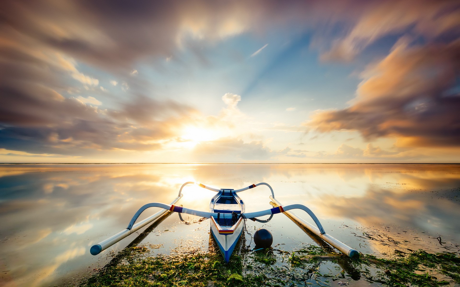 A traditional outrigger canoe rests on a beach at sunrise. HD Wallpaper