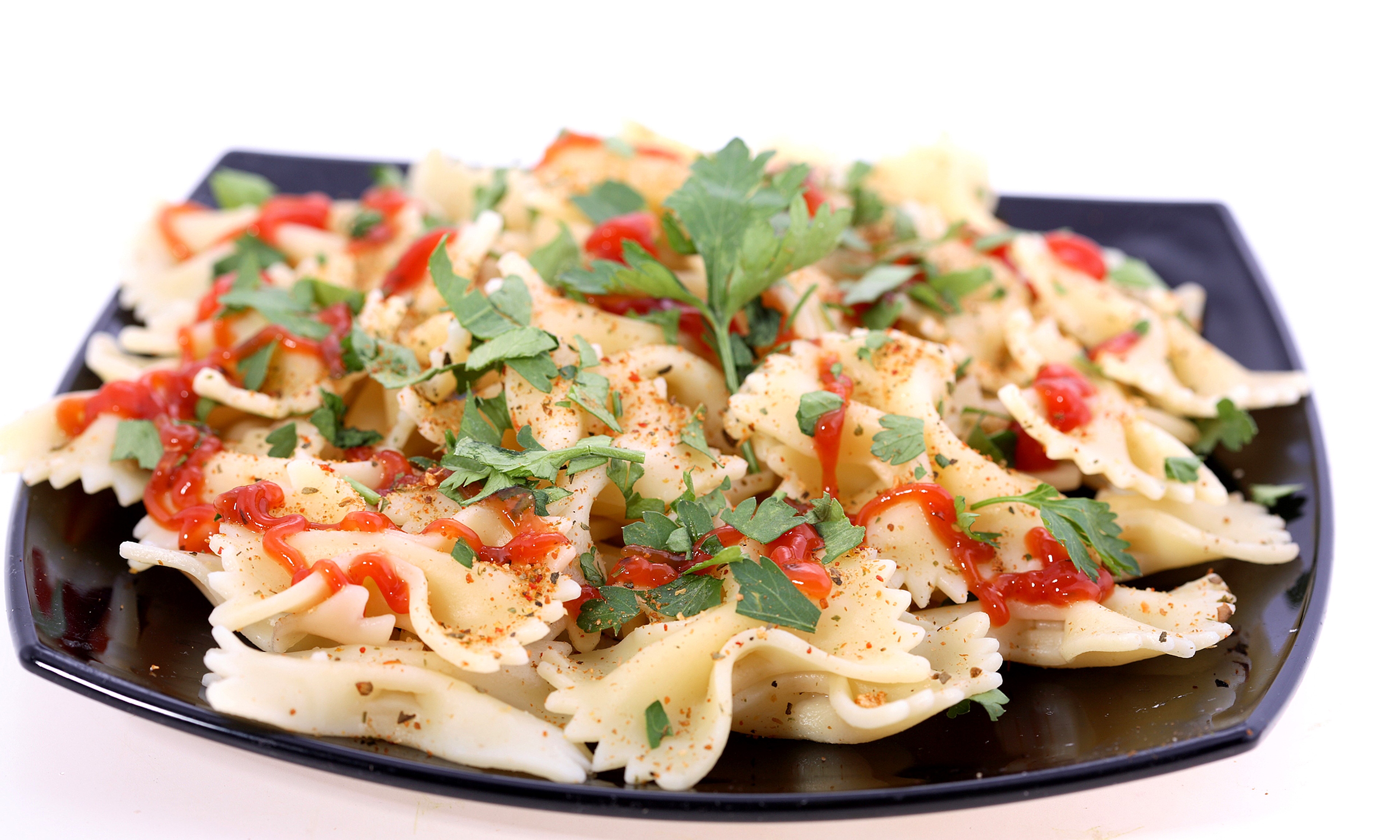 Farfalle pasta with ketchup and parsley on a black plate HD Wallpaper