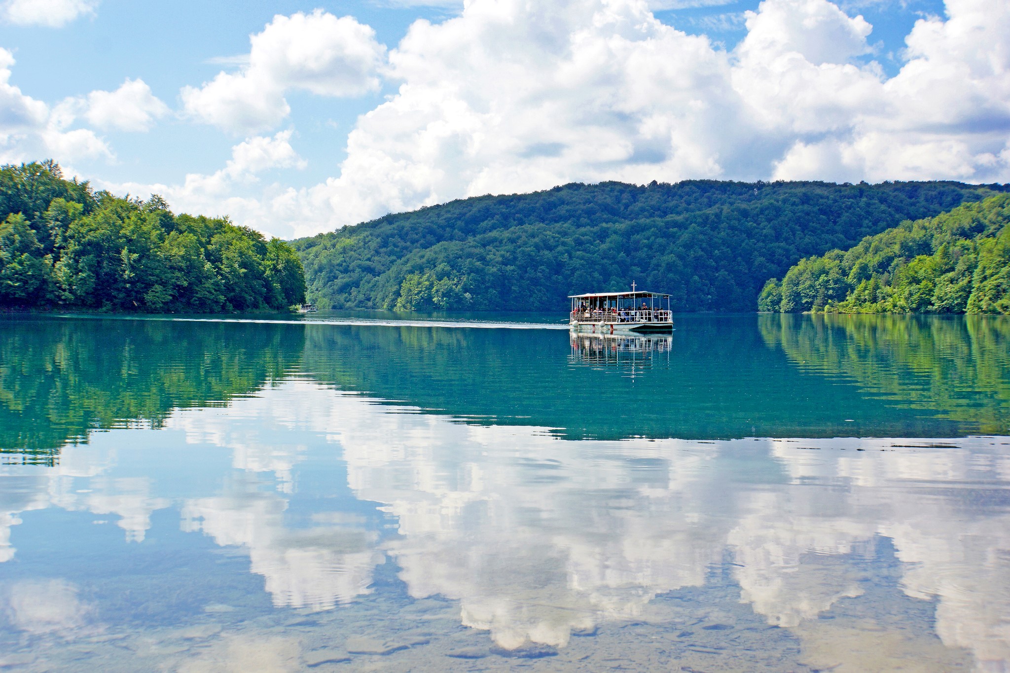 Boat on a clear lake with forested hills and reflections HD Wallpaper