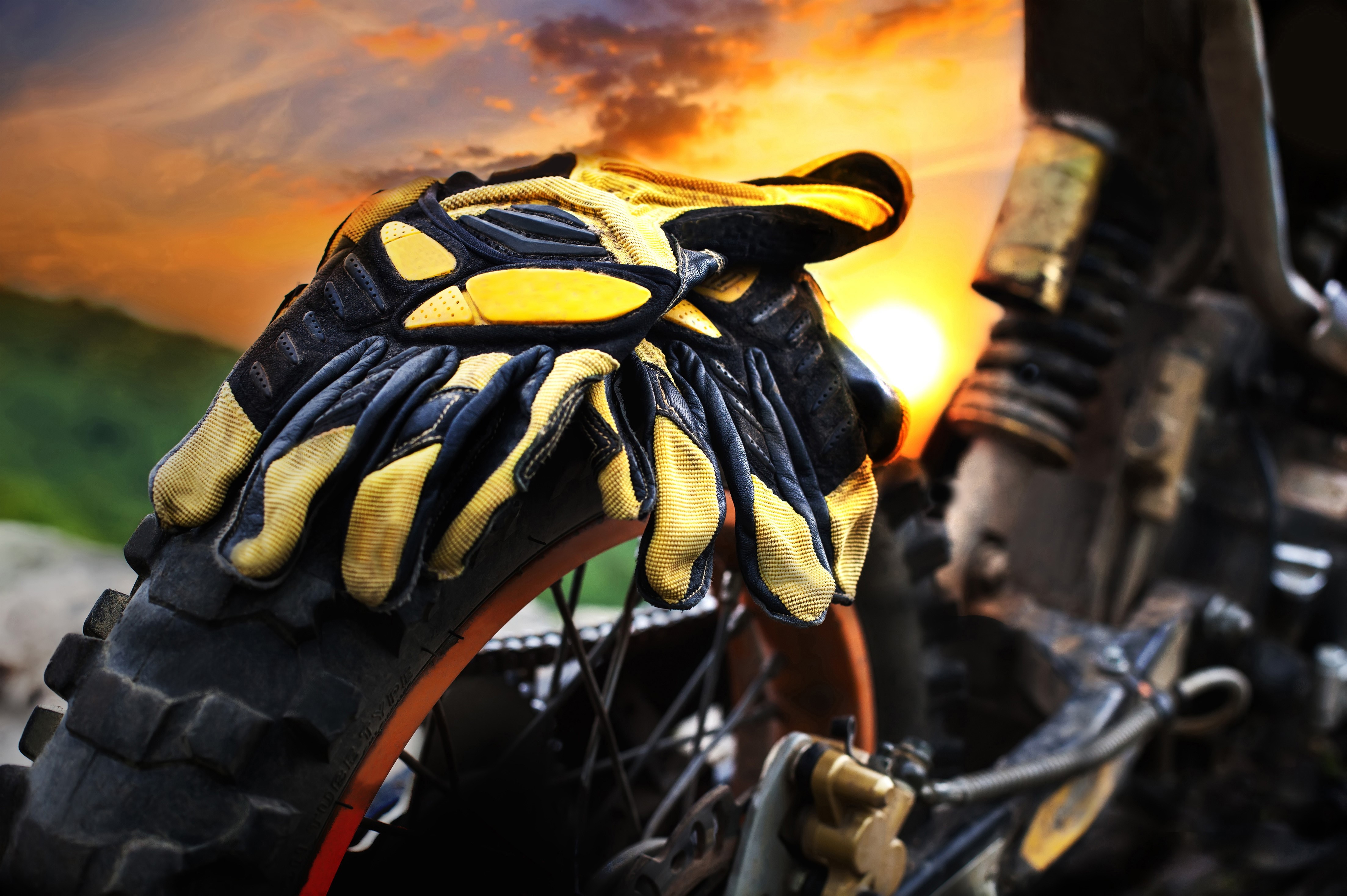 Motocross gloves on a motorcycle tire at sunset HD Wallpaper