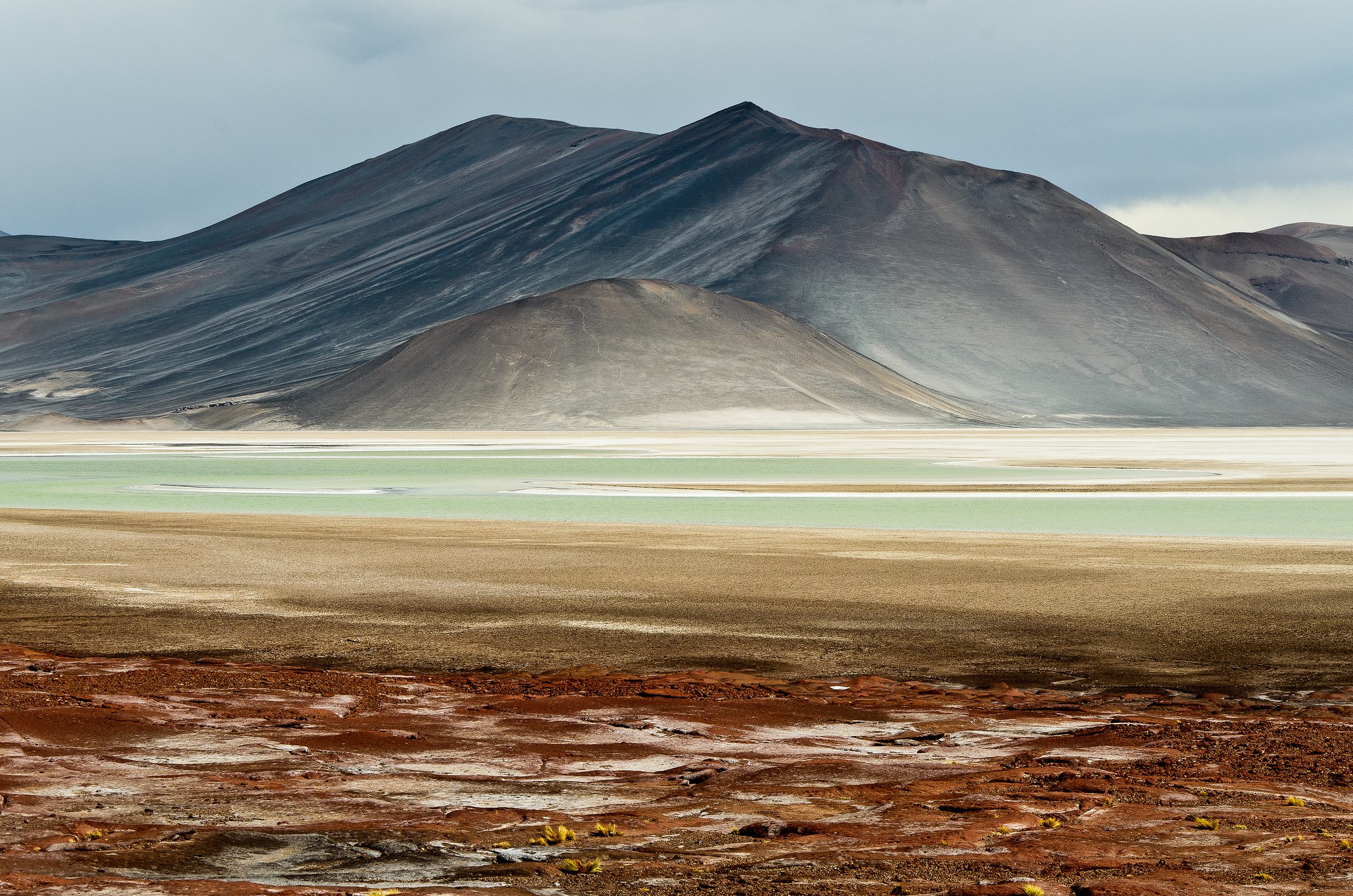 Volcanic mountains and a green lake in a barren landscape HD Wallpaper