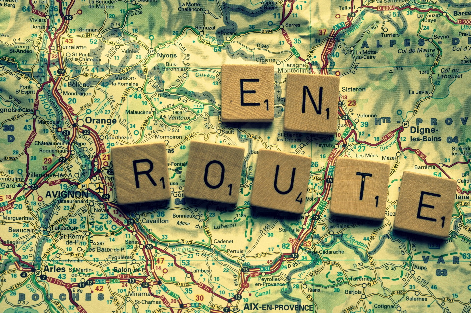 Scrabble tiles spelling 'EN ROUTE' on a map HD Wallpaper