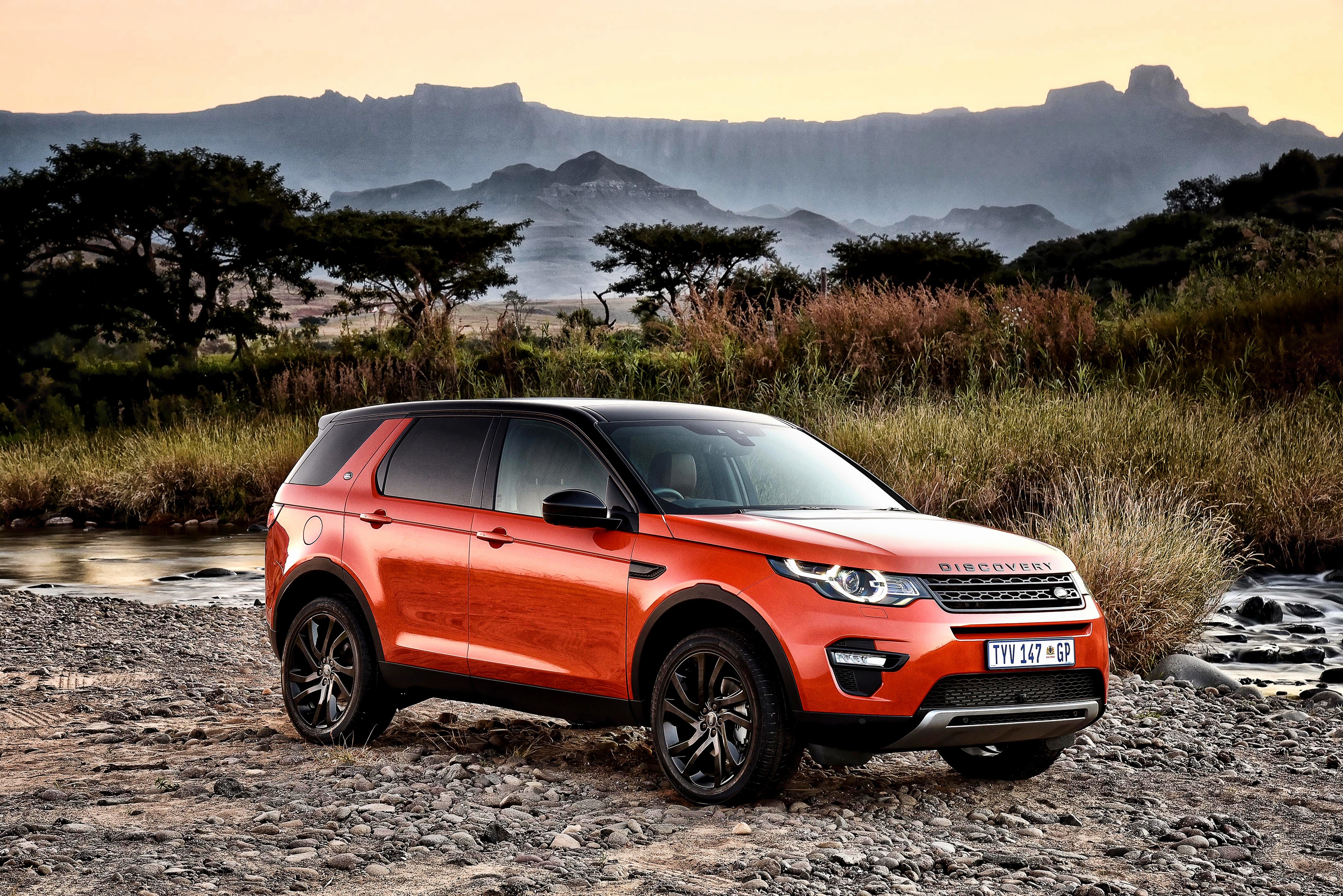 Orange Land Rover Discovery Sport in a rocky landscape HD Wallpaper