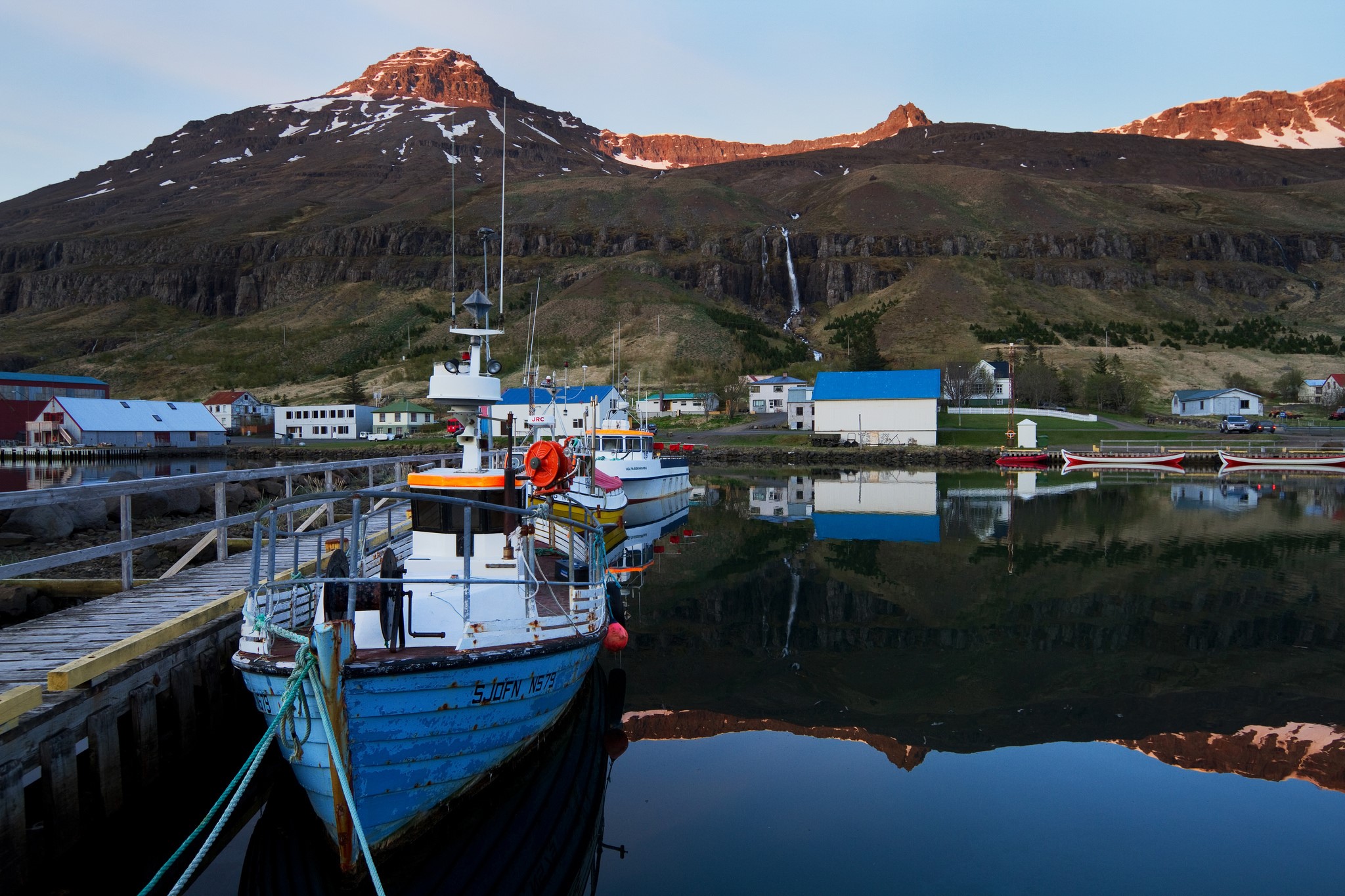 Boats docked in a harbor with a mountain and waterfall in Iceland HD Wallpaper