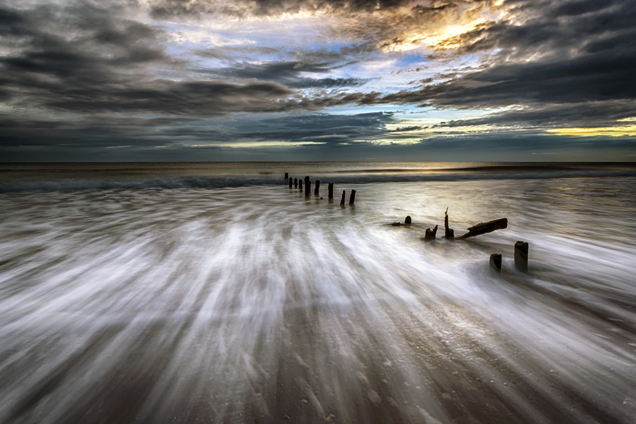 Ocean waves crashing on beach with wooden posts HD Wallpaper