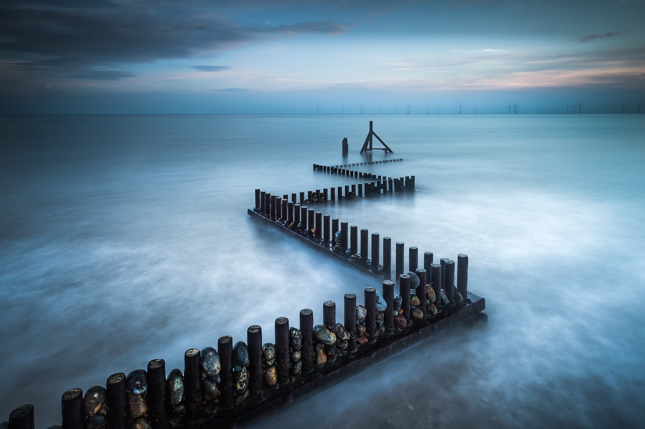 Wooden breakwaters in the sea at dusk, England HD Wallpaper