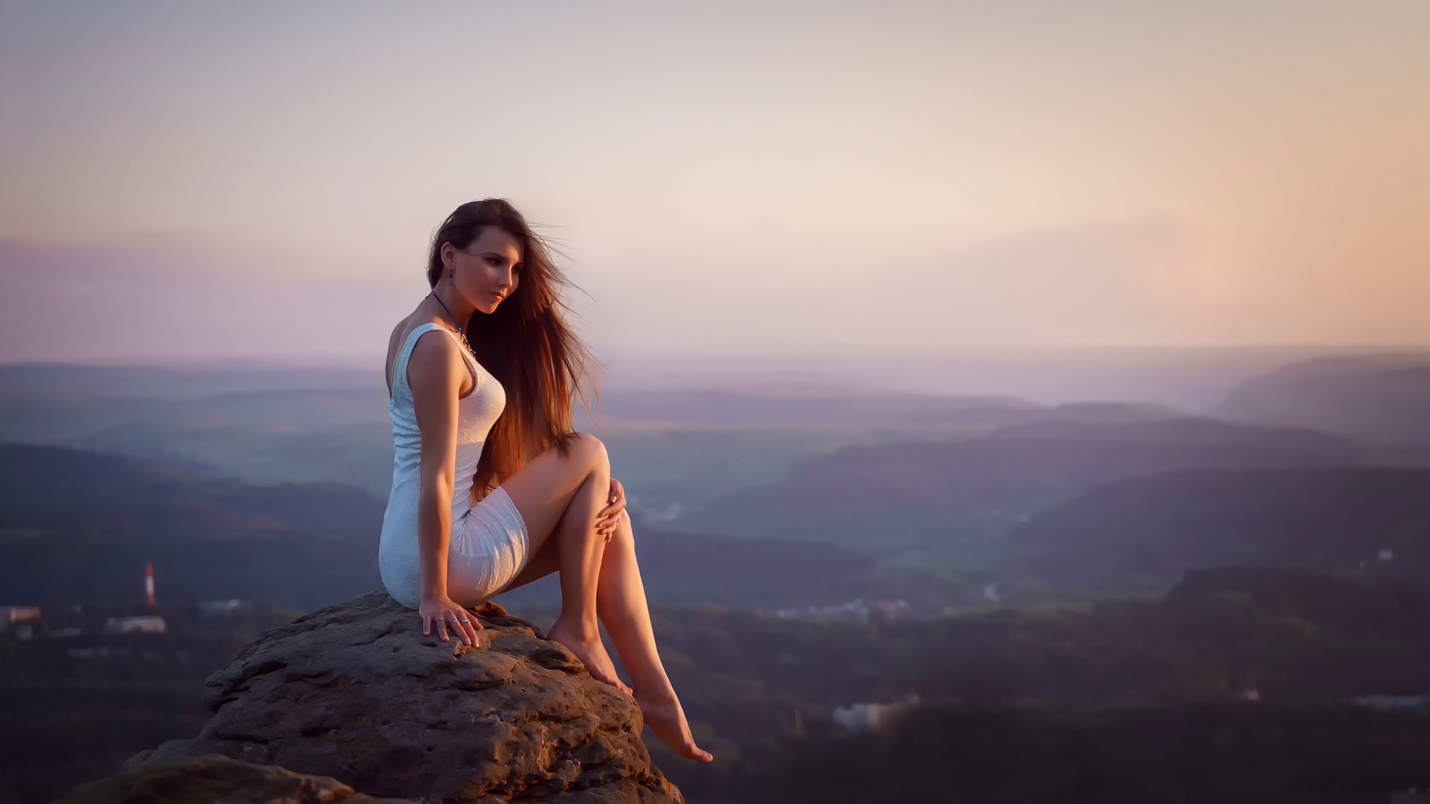 Woman in white dress sitting on a rock overlooking a valley HD Wallpaper
