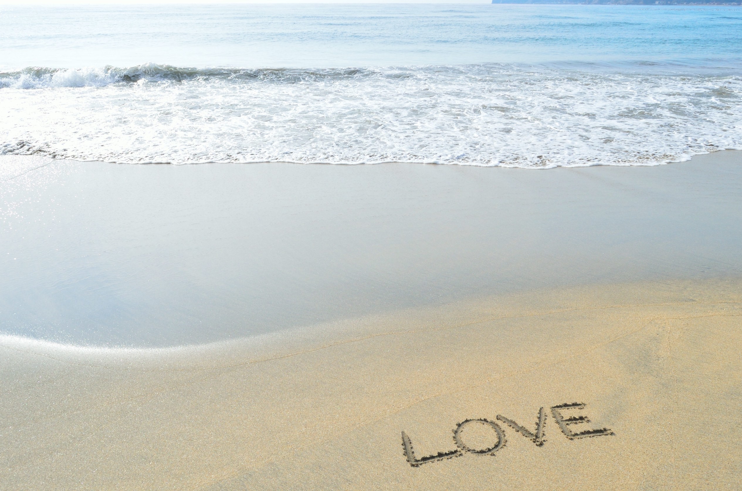 The word LOVE written in the sand on a beach with waves. HD Wallpaper