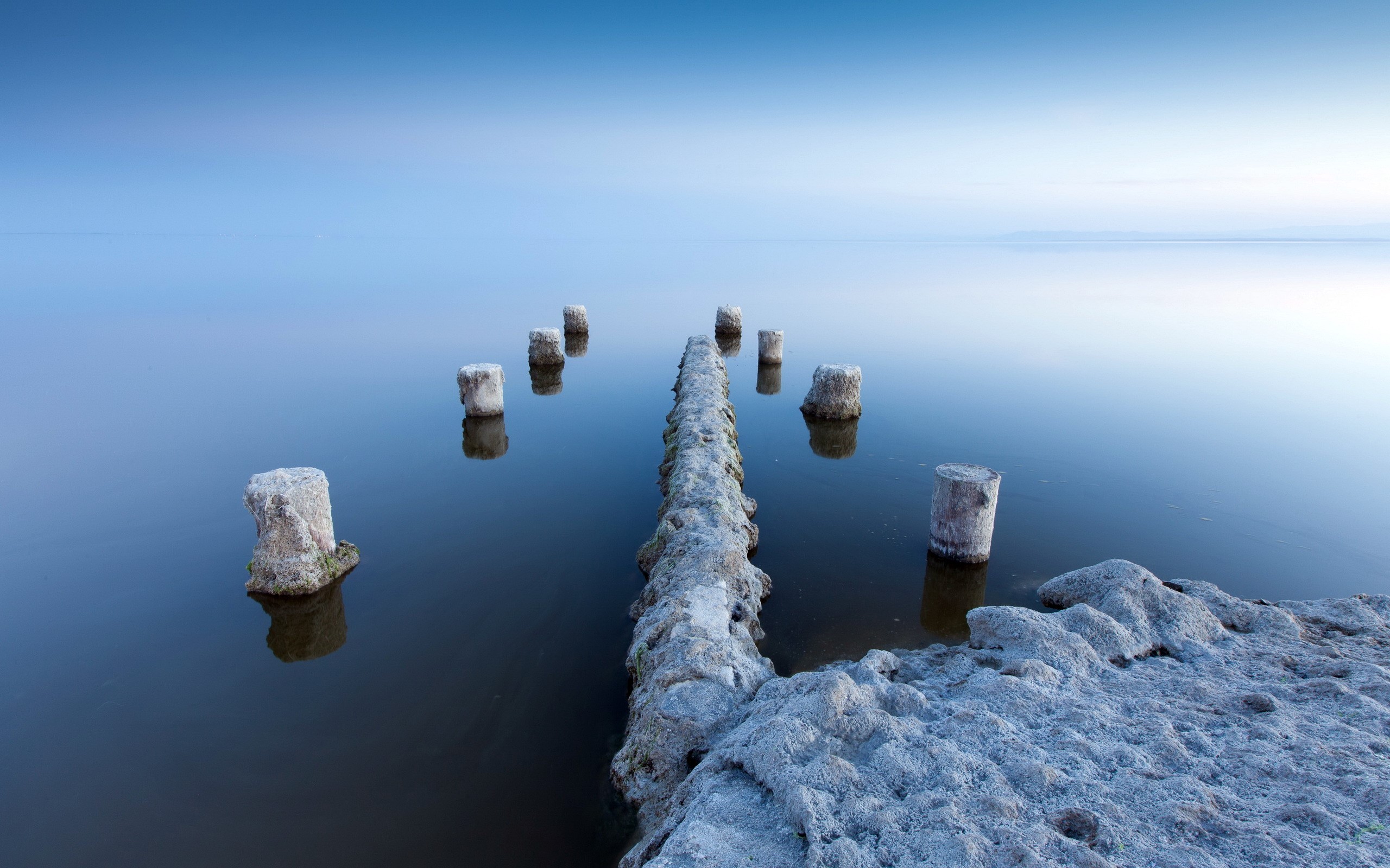 Wooden posts in calm water at sunrise HD Wallpaper
