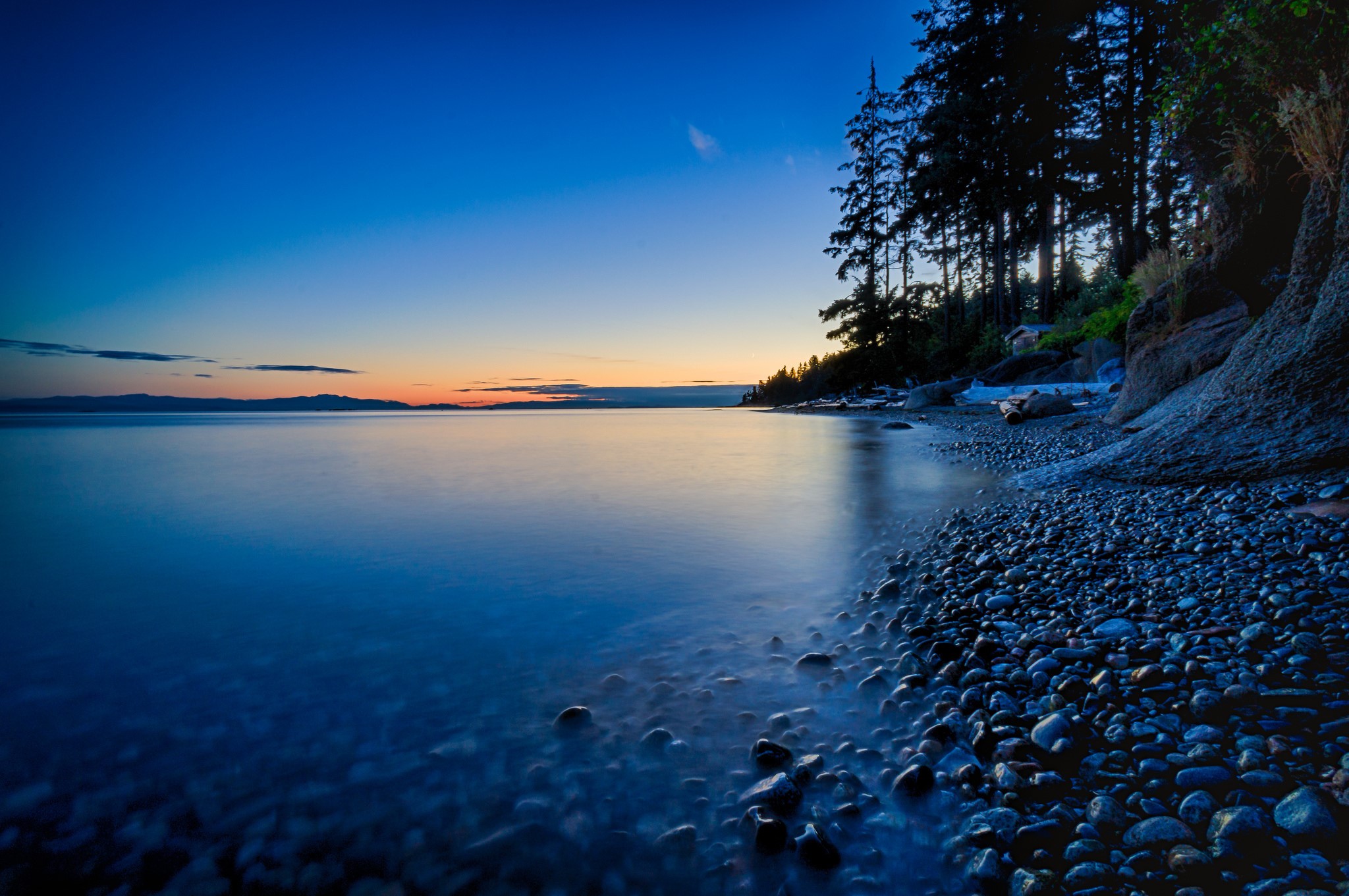 Rocky Shoreline at Dusk with Calm Water HD Wallpaper