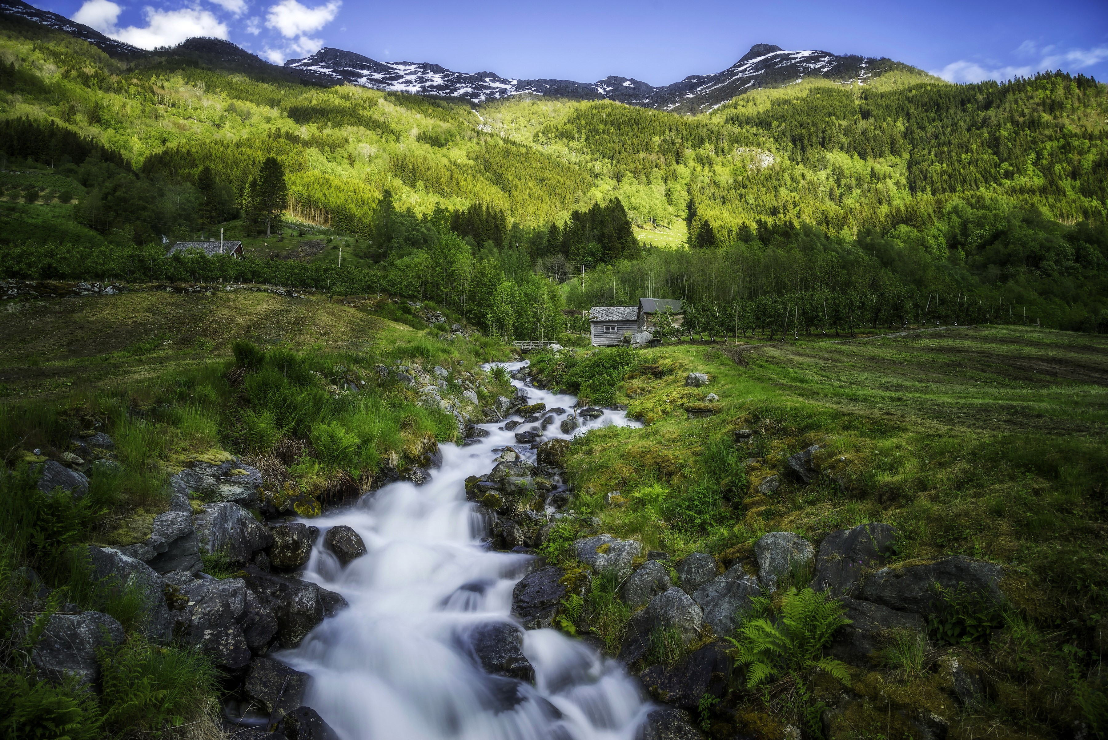 Mountain stream flowing through a green valley with a house HD Wallpaper