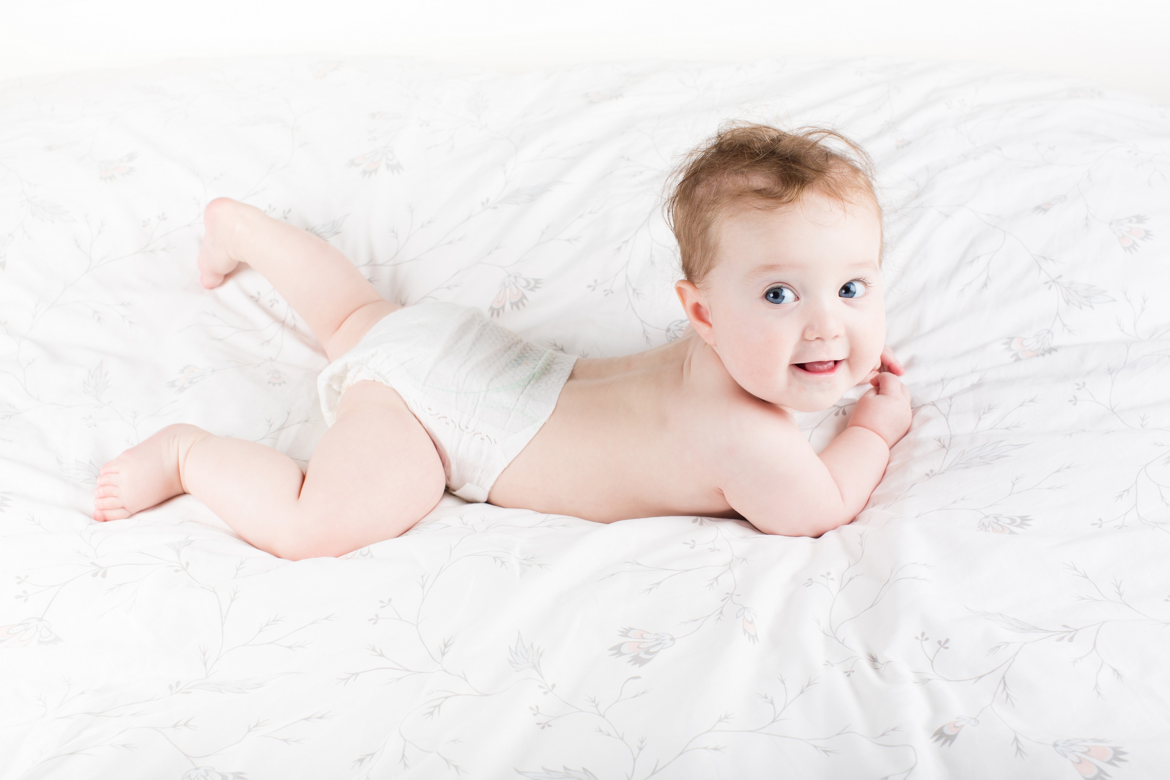 Baby in a diaper lying on a patterned bed HD Wallpaper