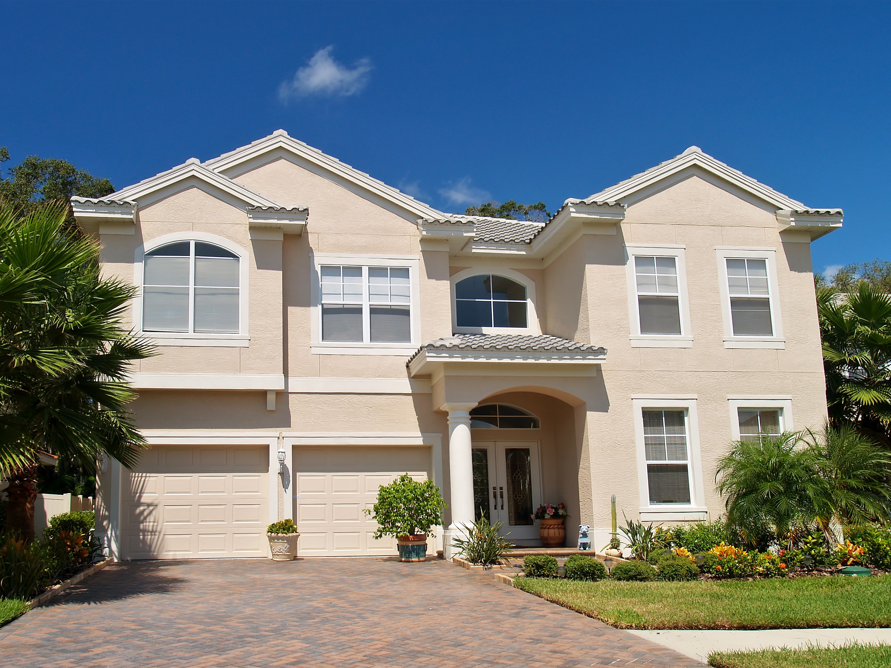 Two-story beige stucco house with garage and palm trees HD Wallpaper