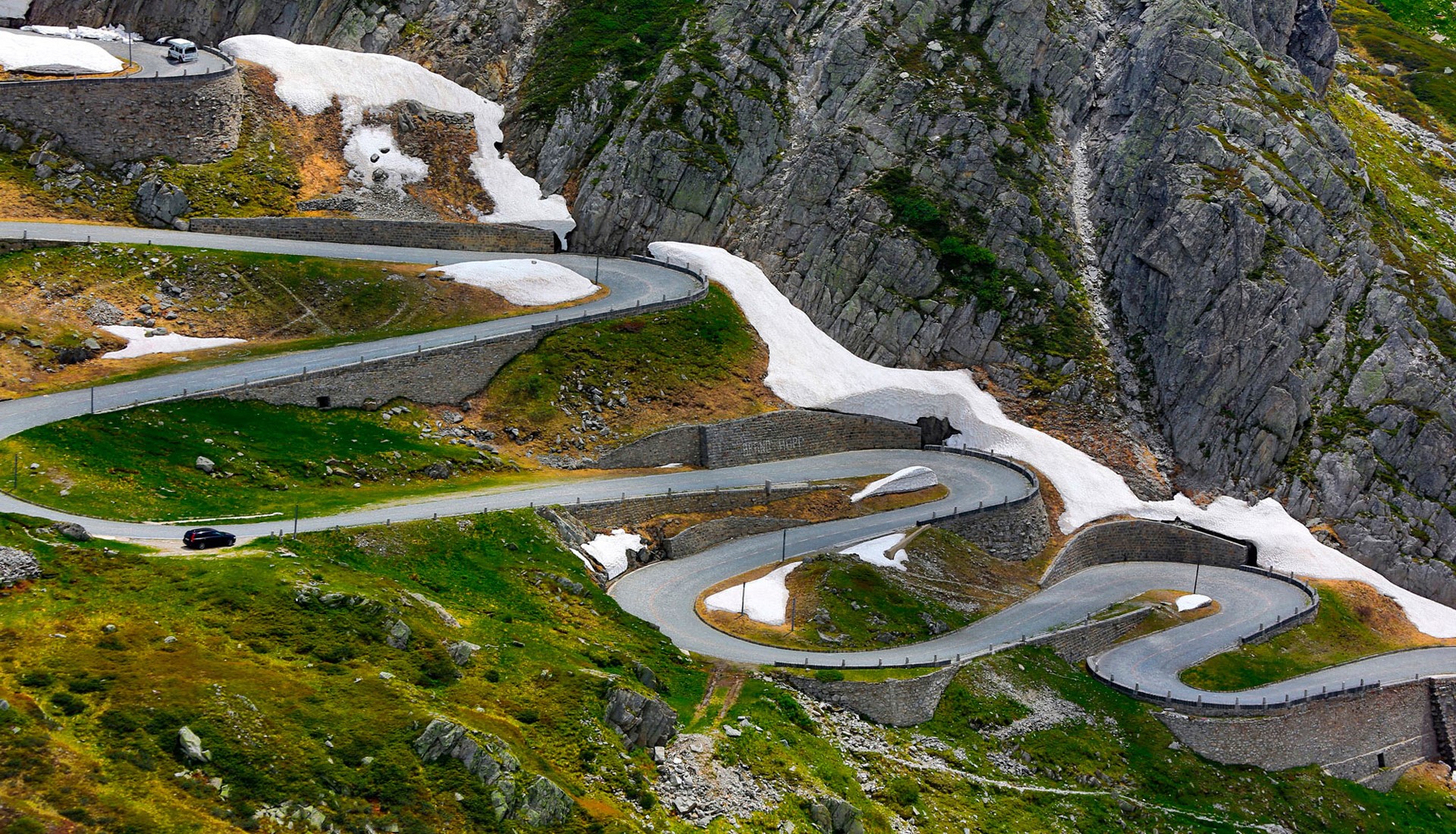 Winding mountain road with snow patches HD Wallpaper