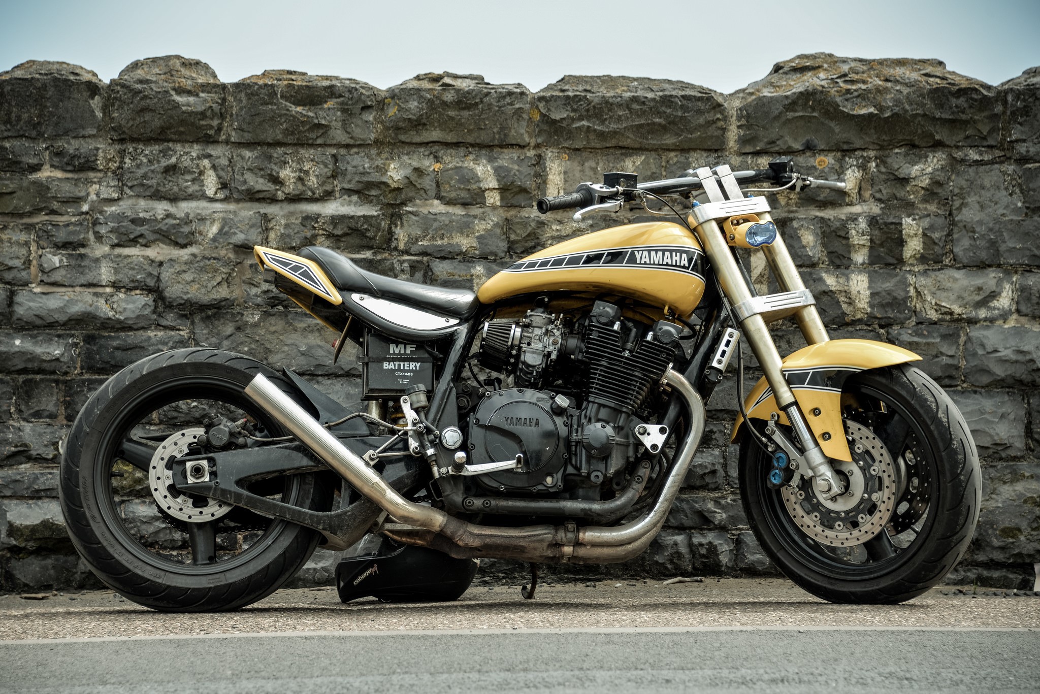 Yellow Yamaha motorcycle parked against a stone wall HD Wallpaper