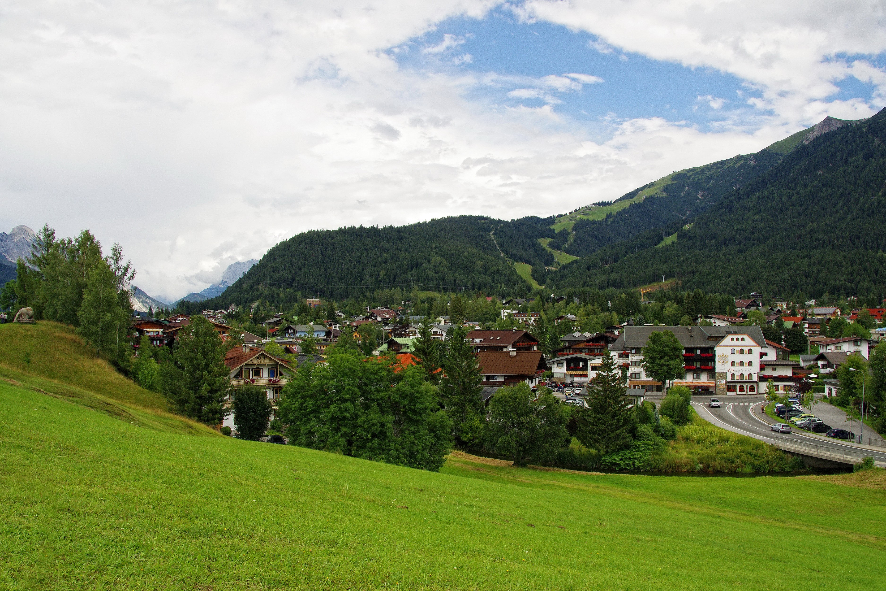 Village nestled in Austrian Alps with green meadows HD Wallpaper