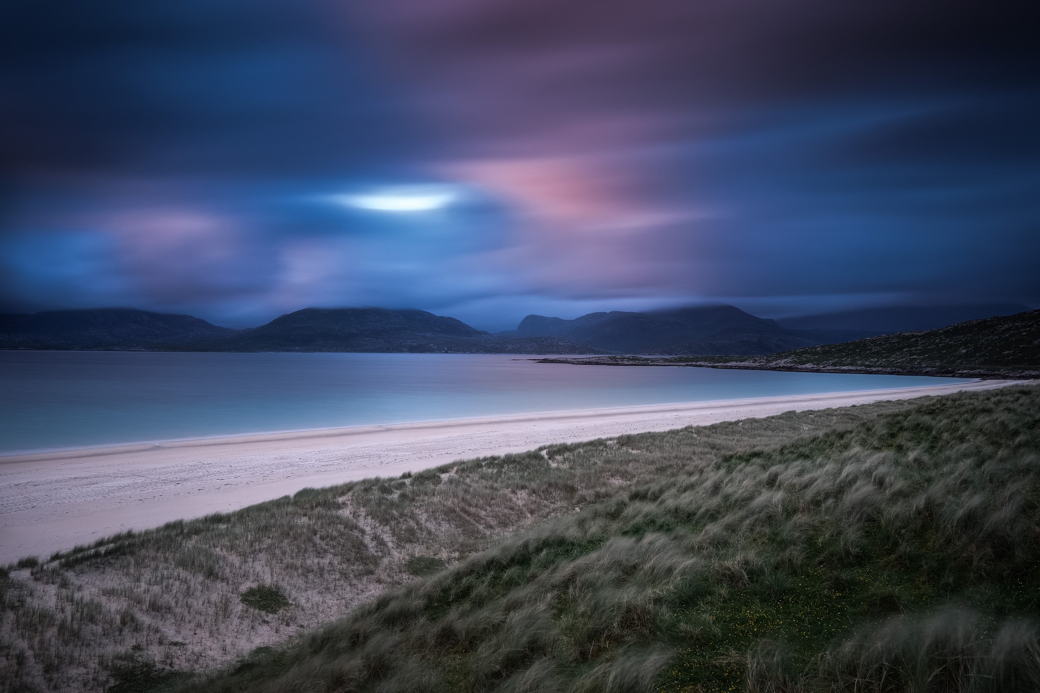 Beach with dunes and mountains under a cloudy sky HD Wallpaper