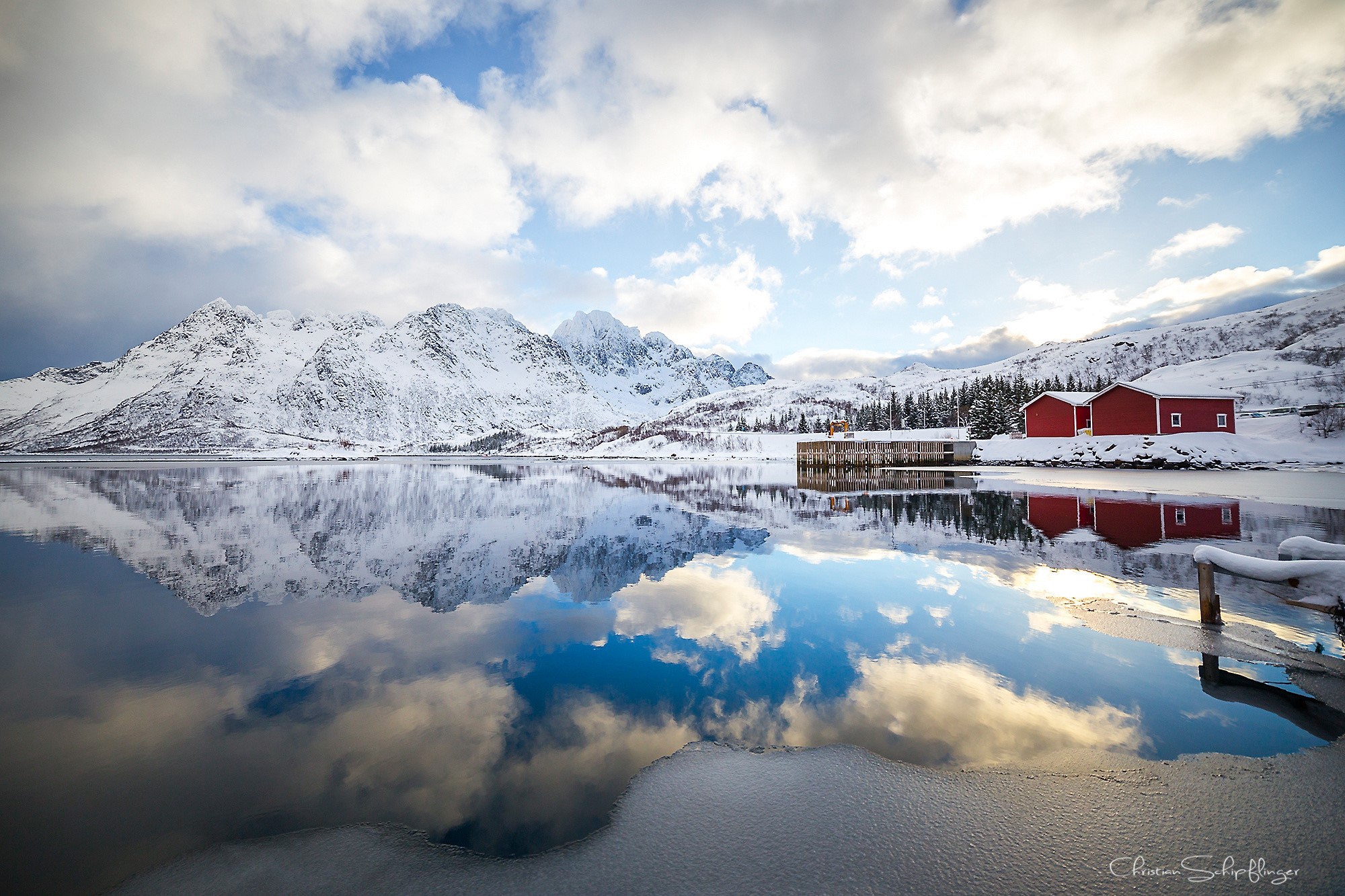 Snowy mountains reflected in a calm lake with red houses in Norway HD Wallpaper