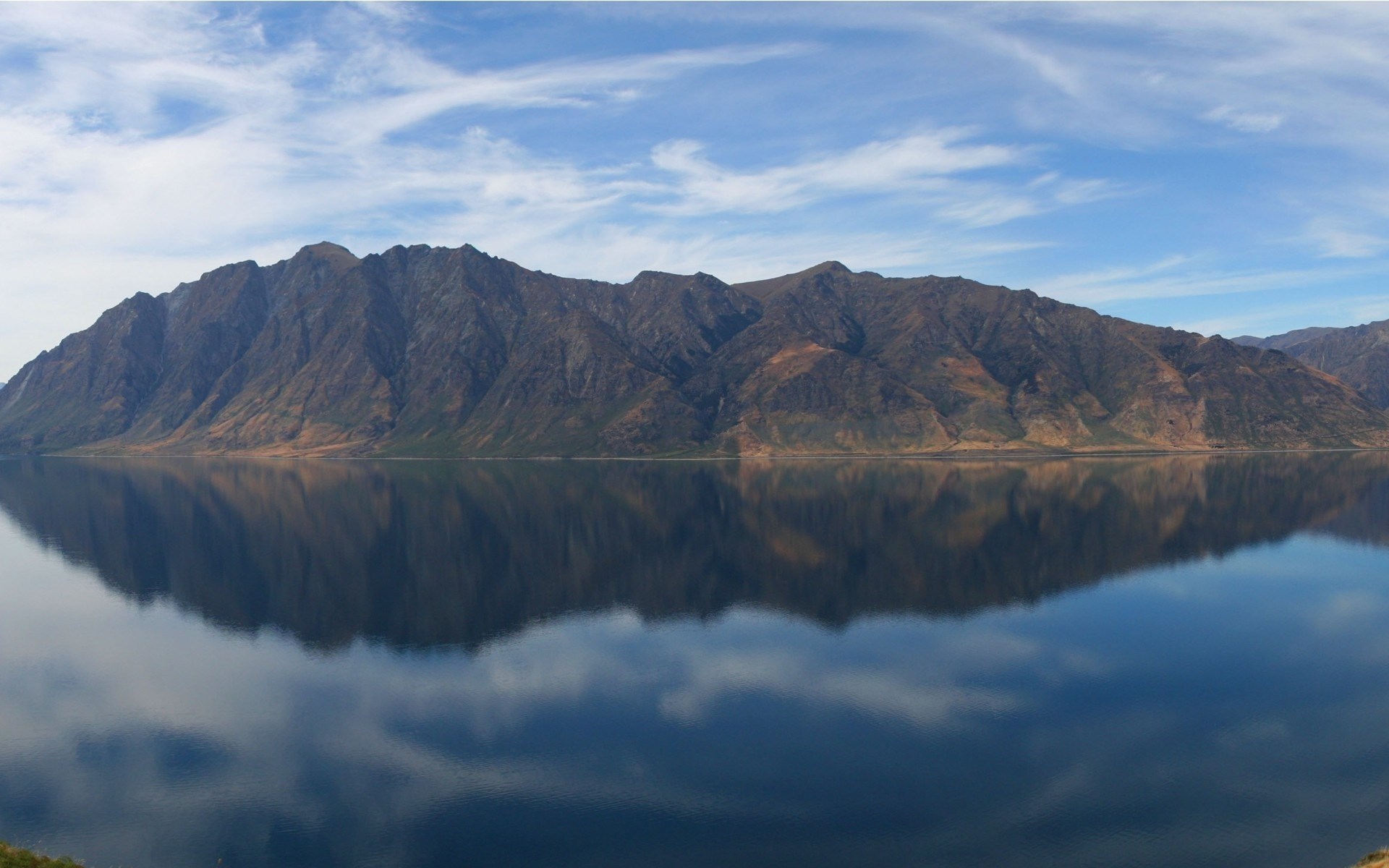 Mountain range reflected in a calm lake under a cloudy sky HD Wallpaper