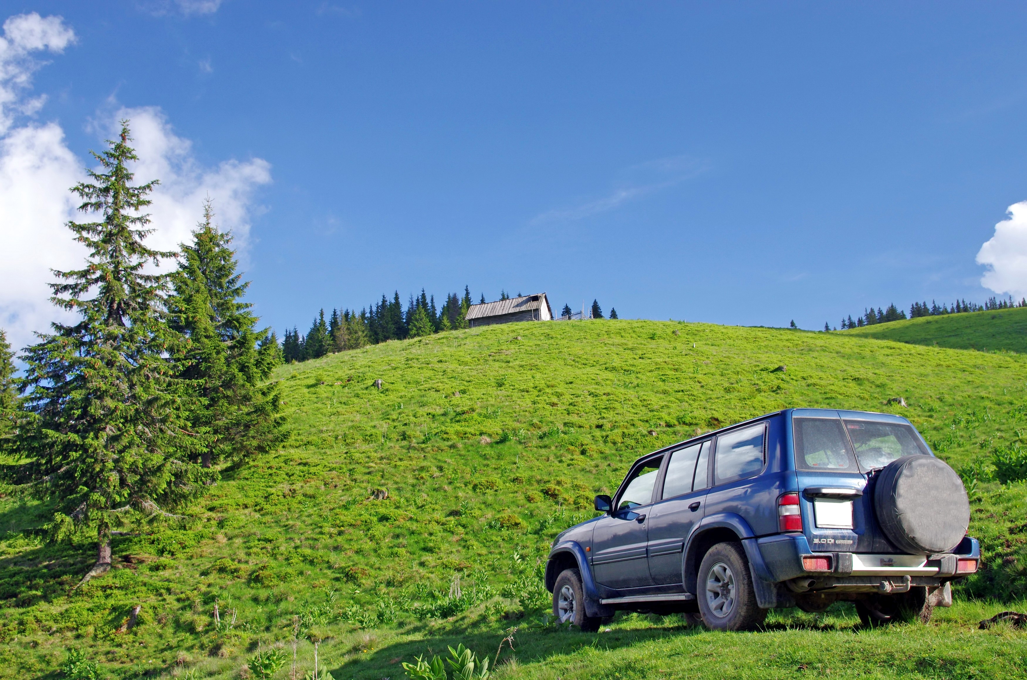 Blue SUV parked on a grassy hill with trees and a cabin HD Wallpaper