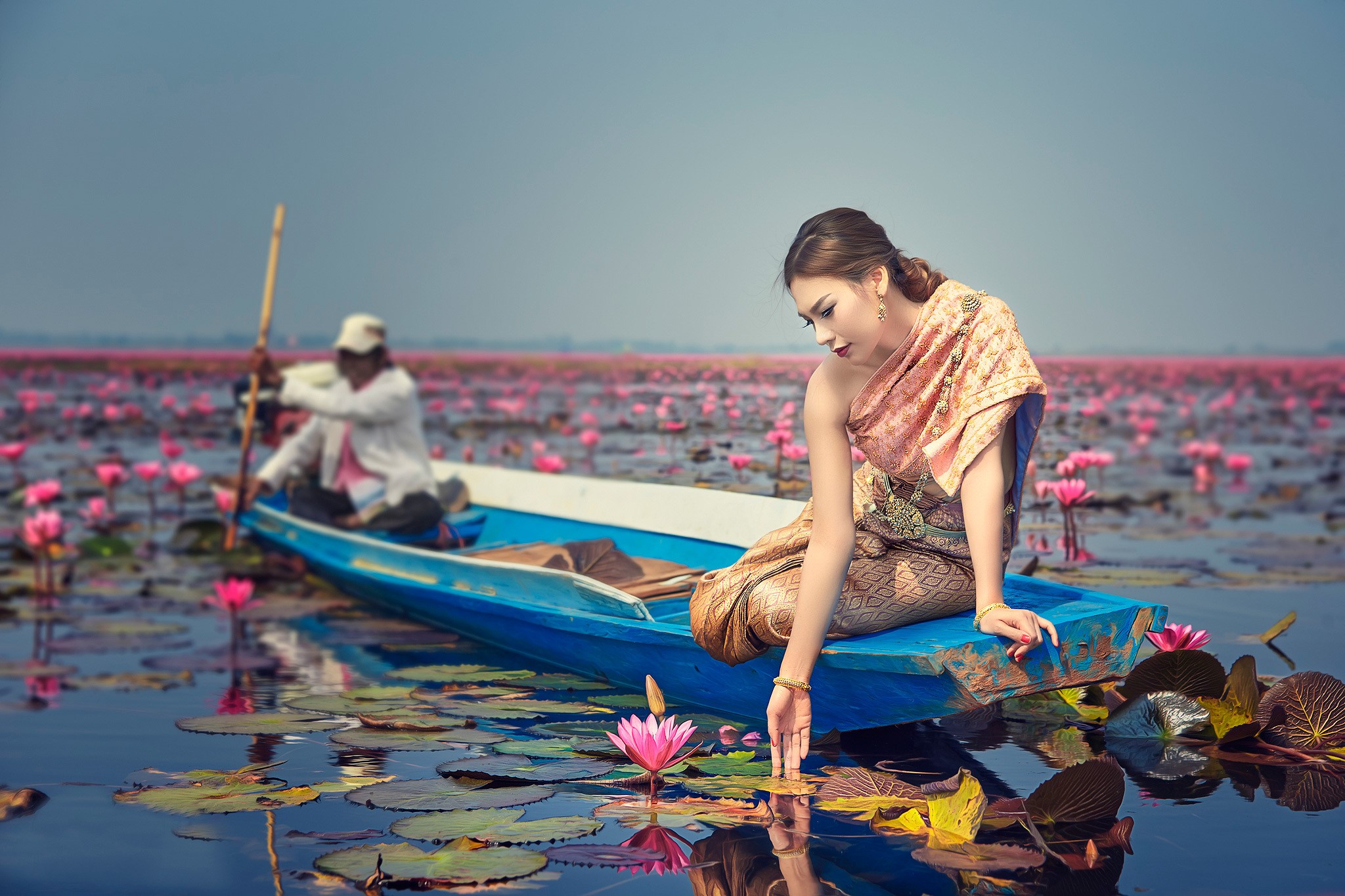 Woman in traditional dress in a boat with lotus flowers HD Wallpaper