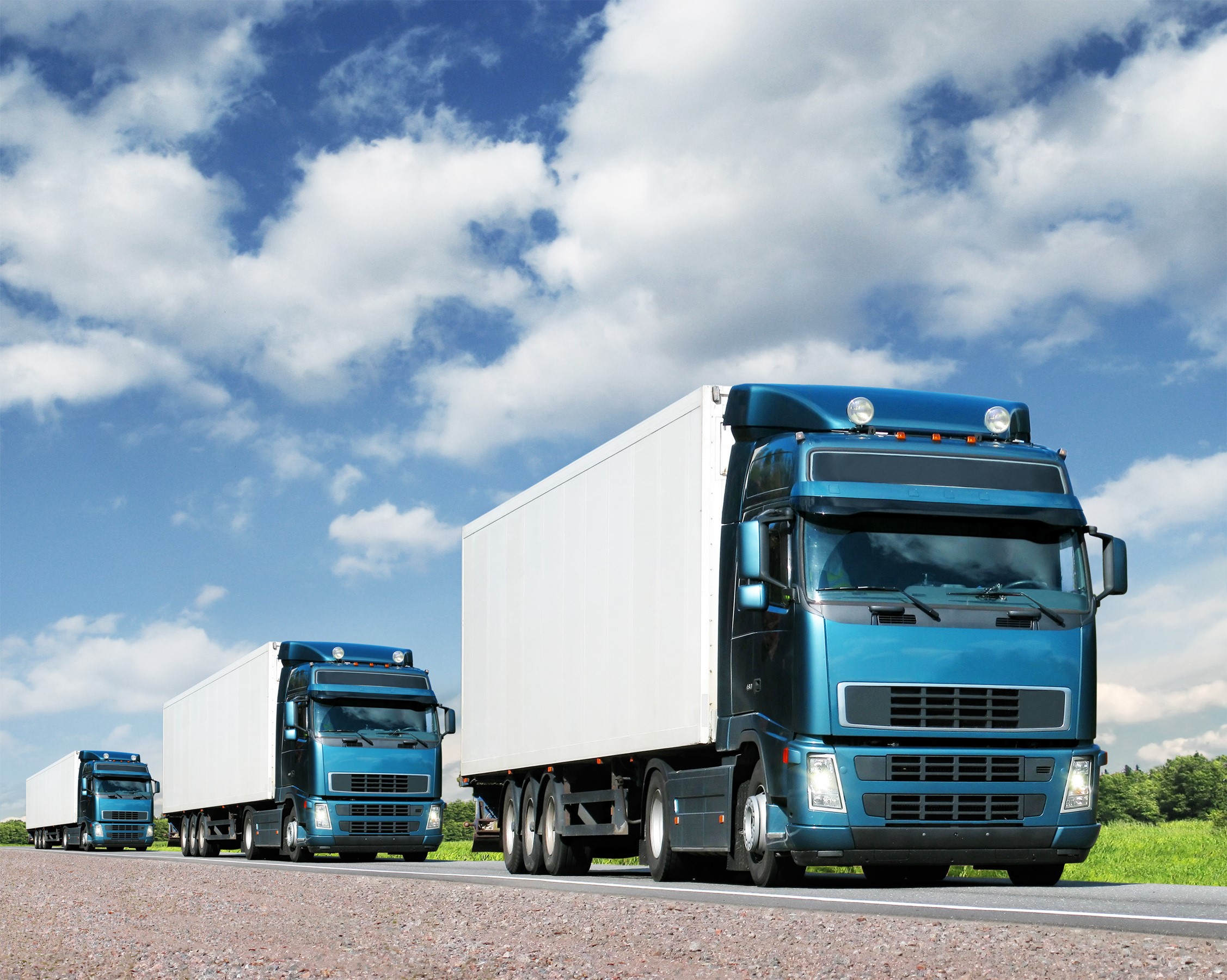 Three blue trucks on a road under a cloudy sky HD Wallpaper