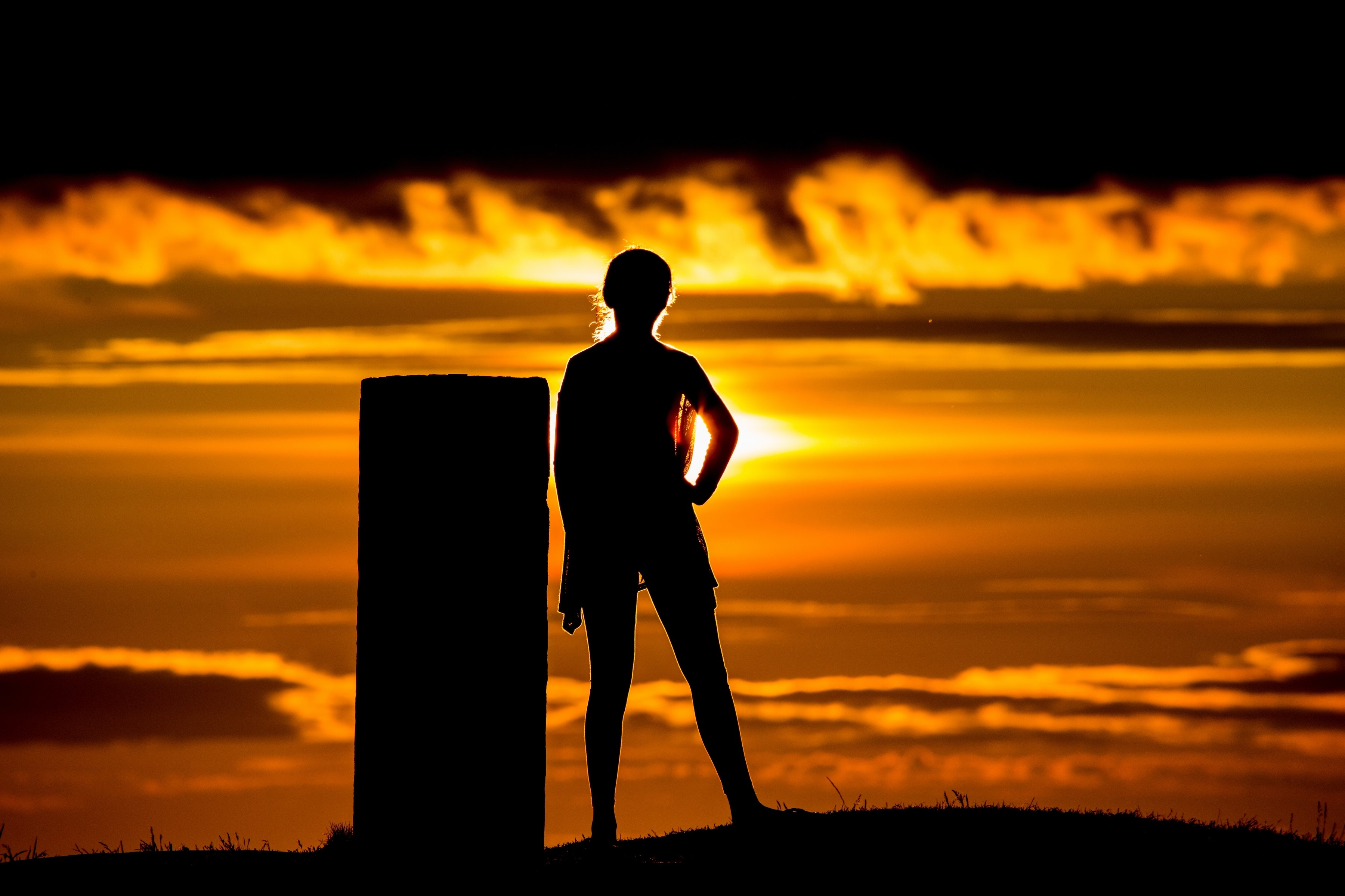 Silhouette of a person standing next to a pillar at sunset HD Wallpaper