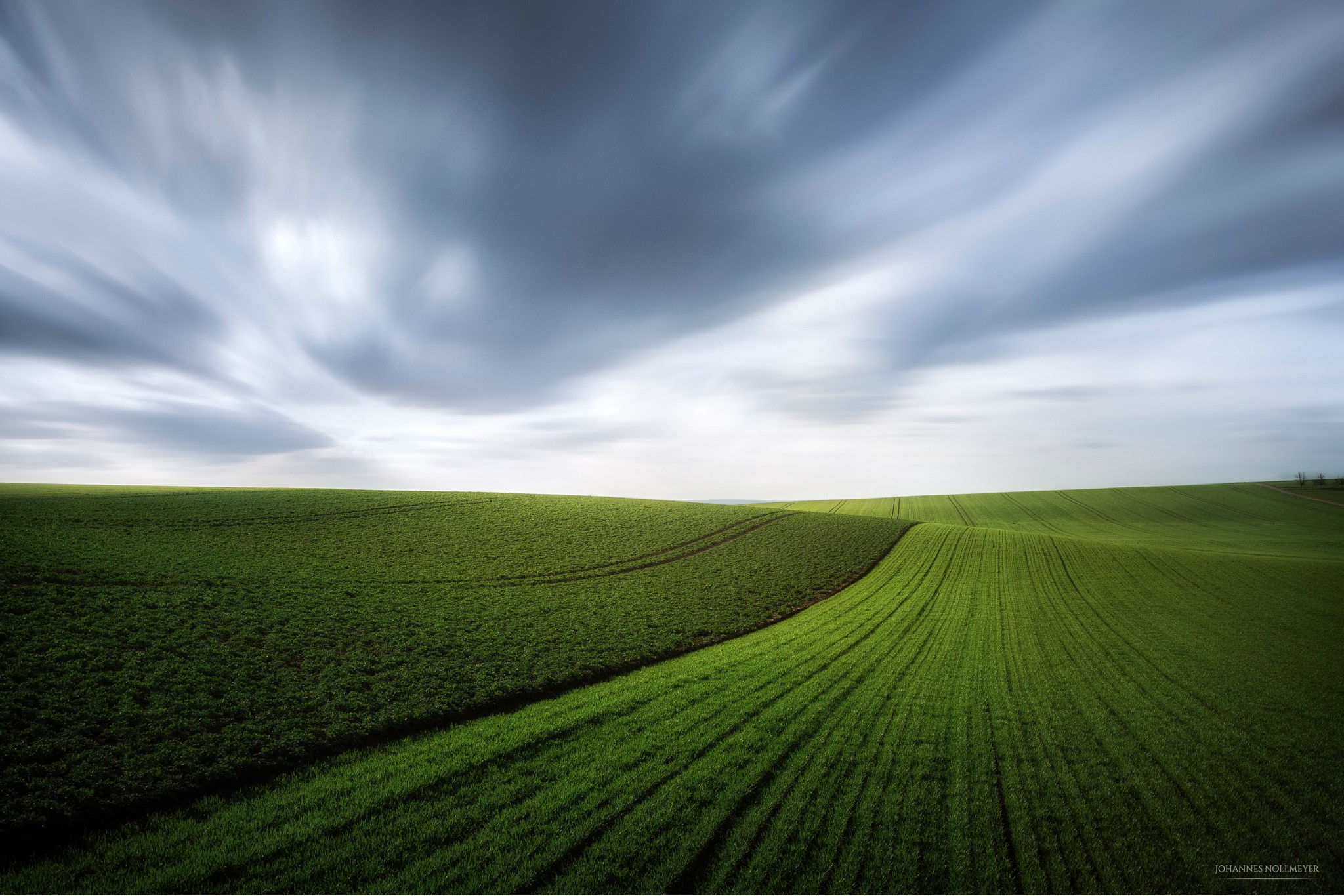 Green rolling fields under a cloudy sky HD Wallpaper