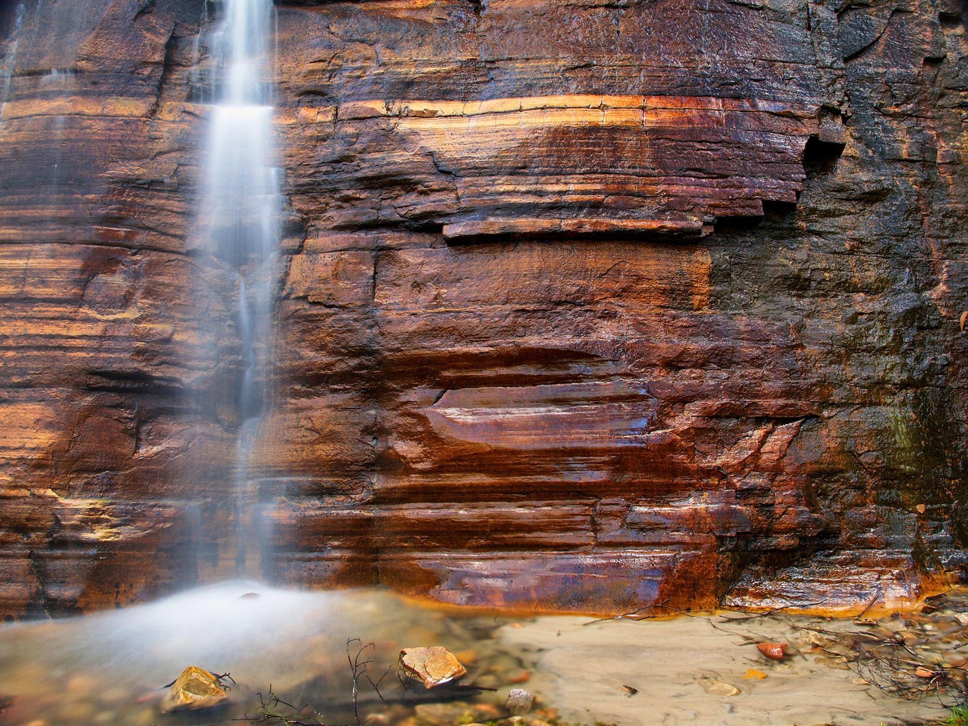 Waterfall cascading down a layered sandstone cliff HD Wallpaper